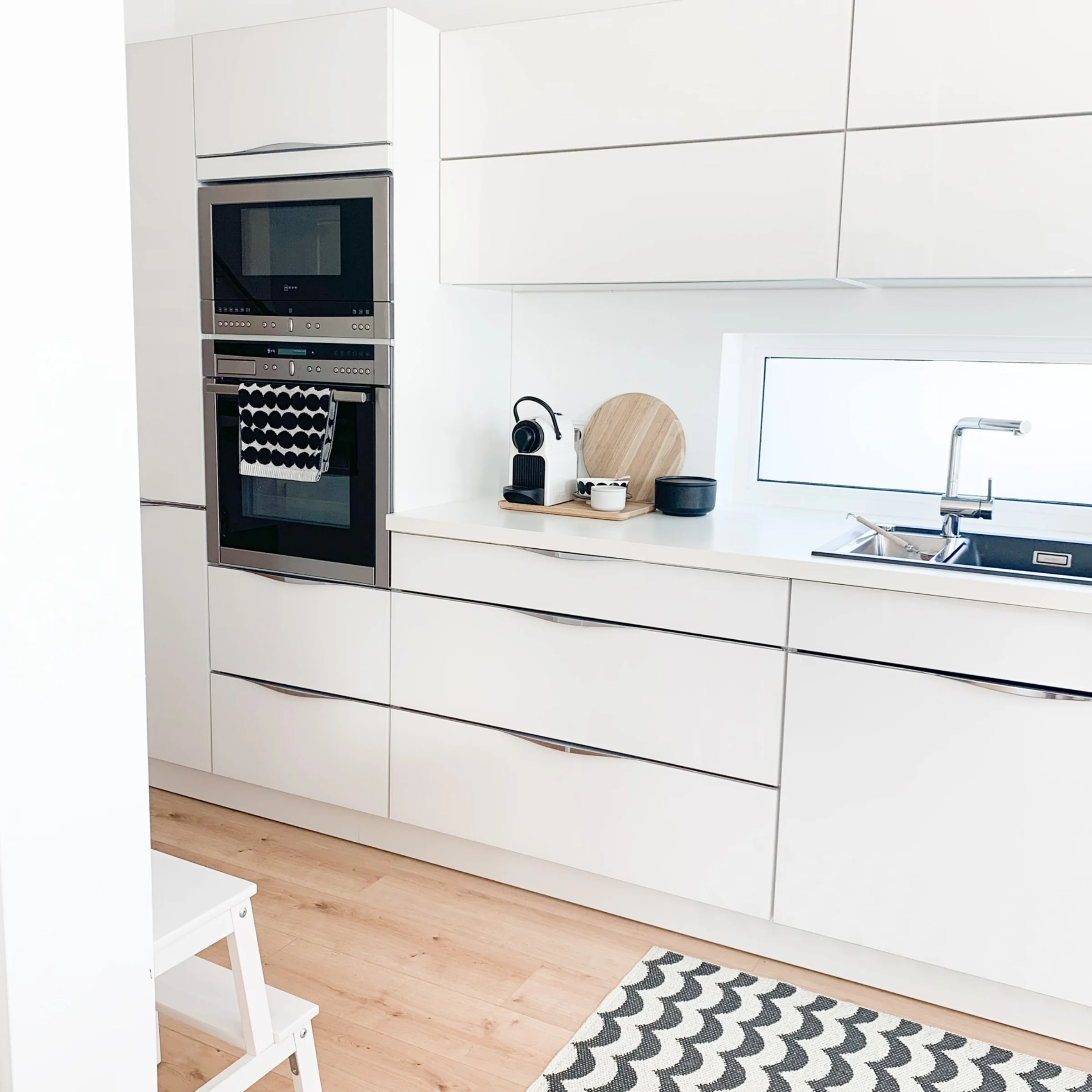 Nowoczesna, jasna kuchnia z białymi szafkami i dywanem, stylowo zaprojektowana przez Nolte Kitchen.