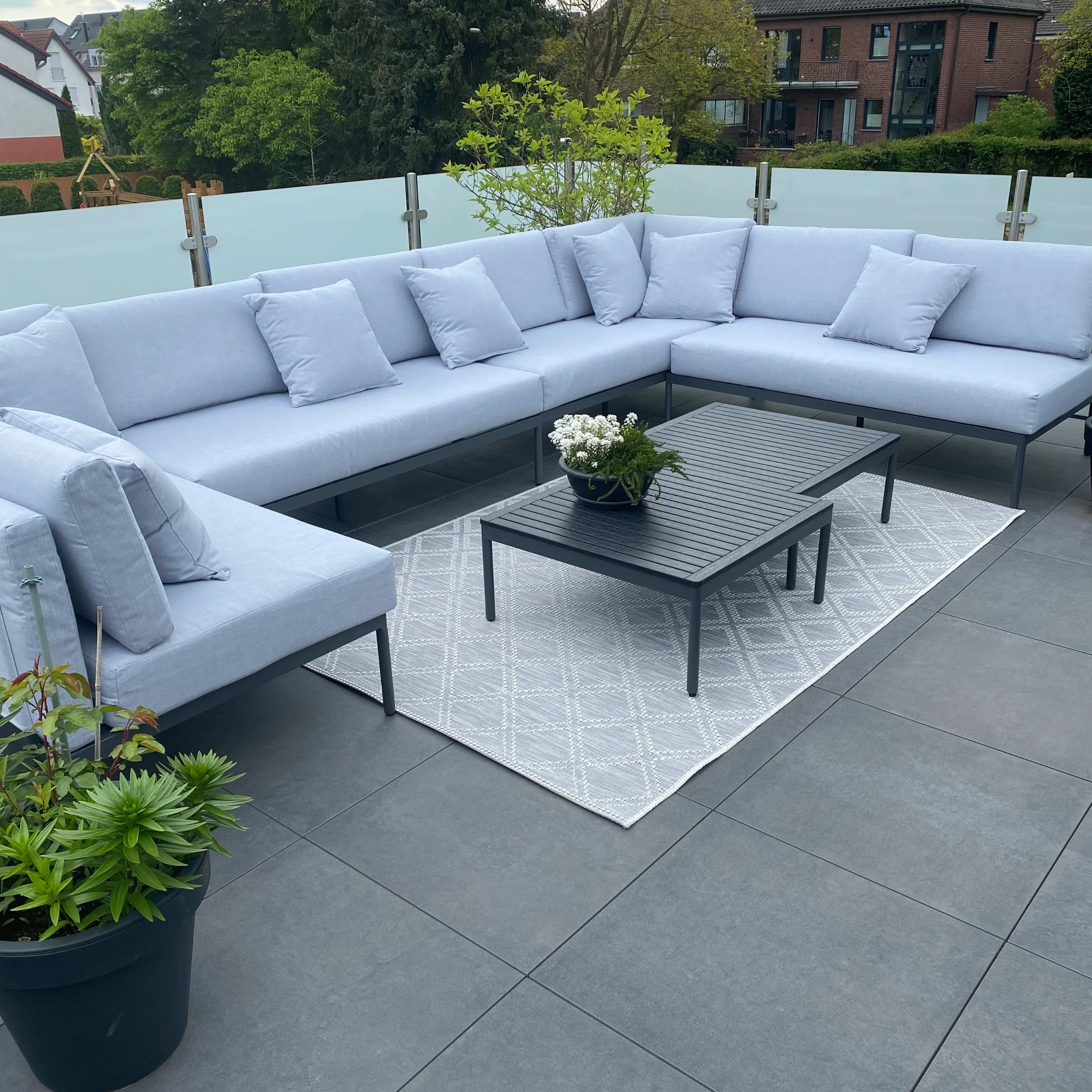 Eine moderne Terrasse mit grauem Loungesofa und Tisch, umgeben von Pflanzen.