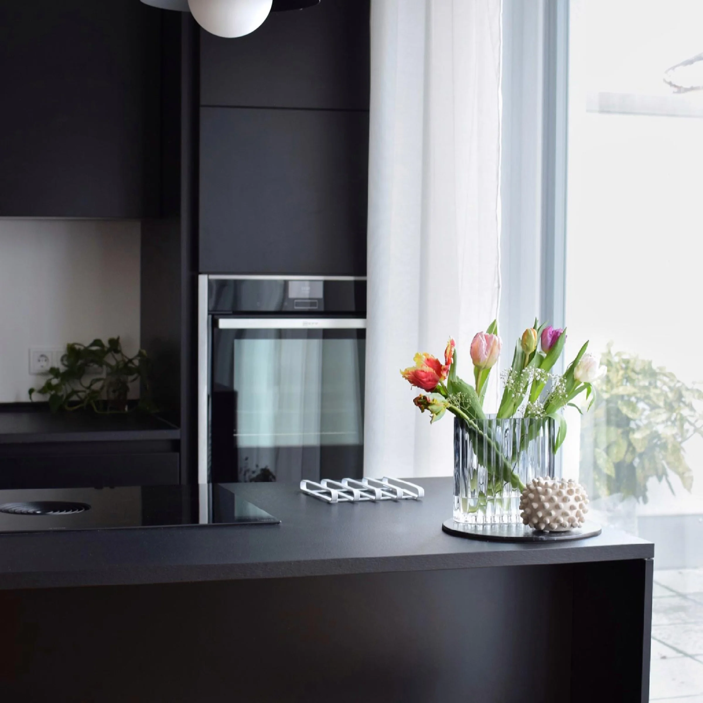 Eine moderne Küche mit schwarzer Arbeitsplatte und bunten Blumen, gestaltet von Nolte Küchen.