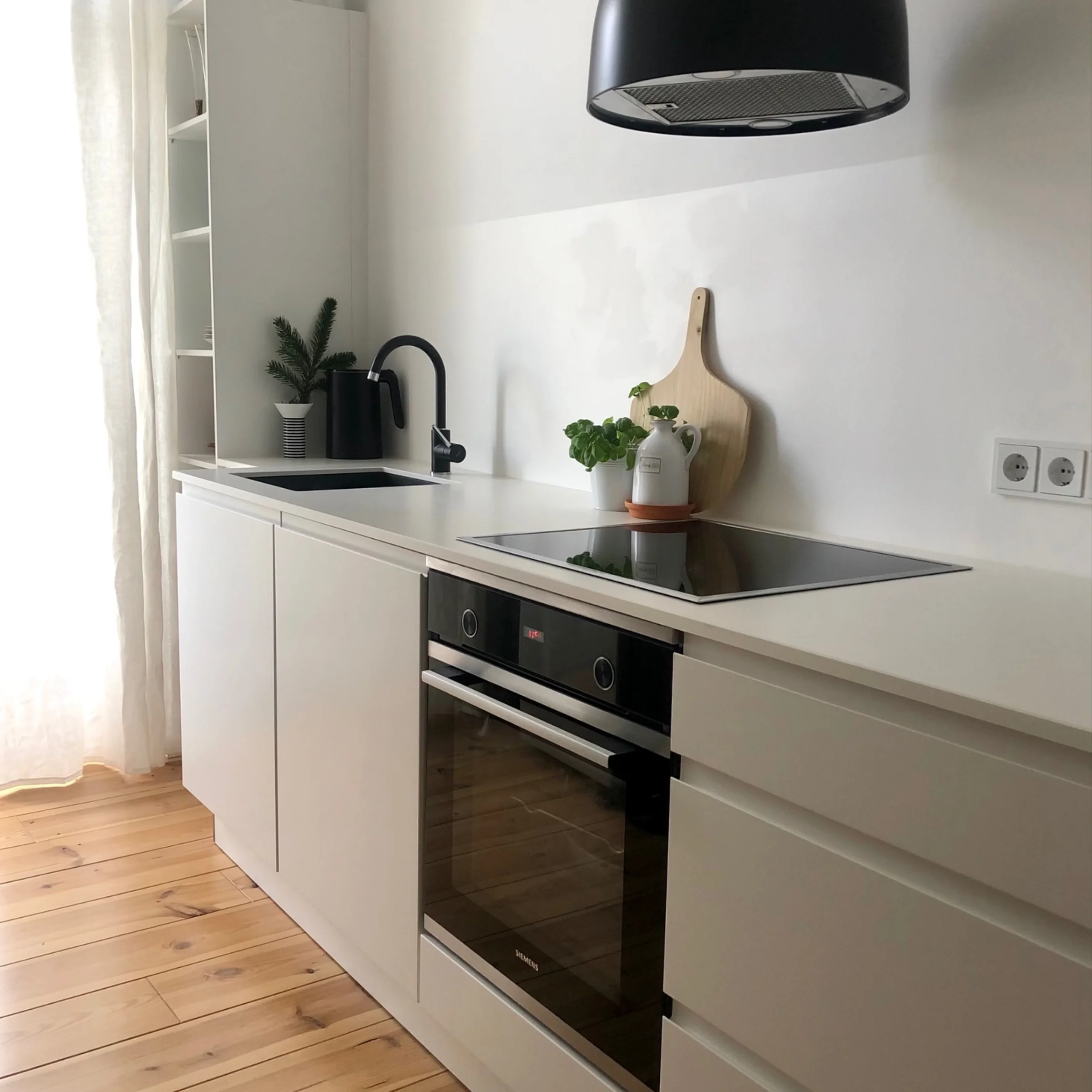 A modern kitchen with white cabinets and wooden floor by Nolte Kitchen.