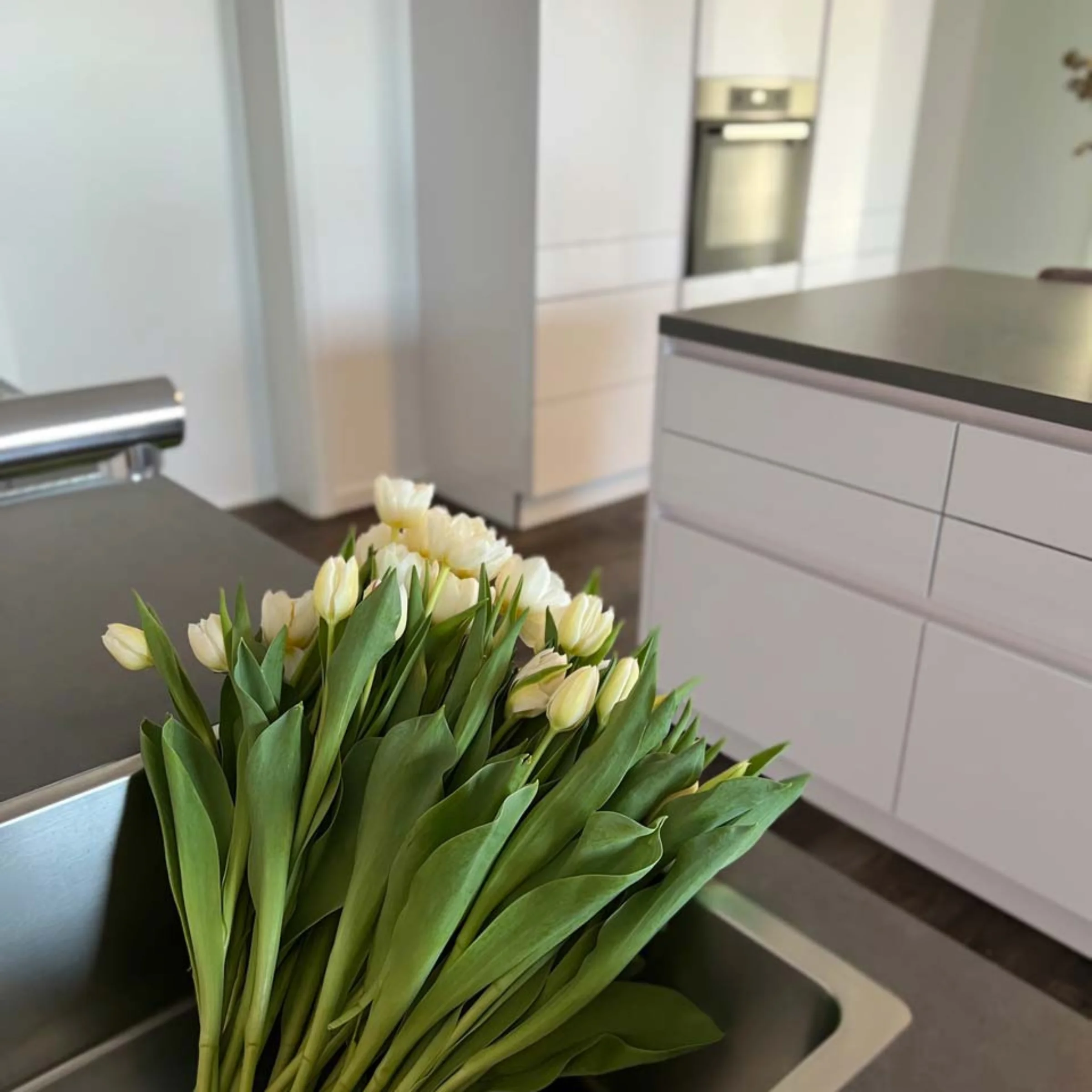 Eine moderne Küche mit weißen Schränken und einem Strauß weißer Tulpen auf der Arbeitsfläche. Nolte Küchen.