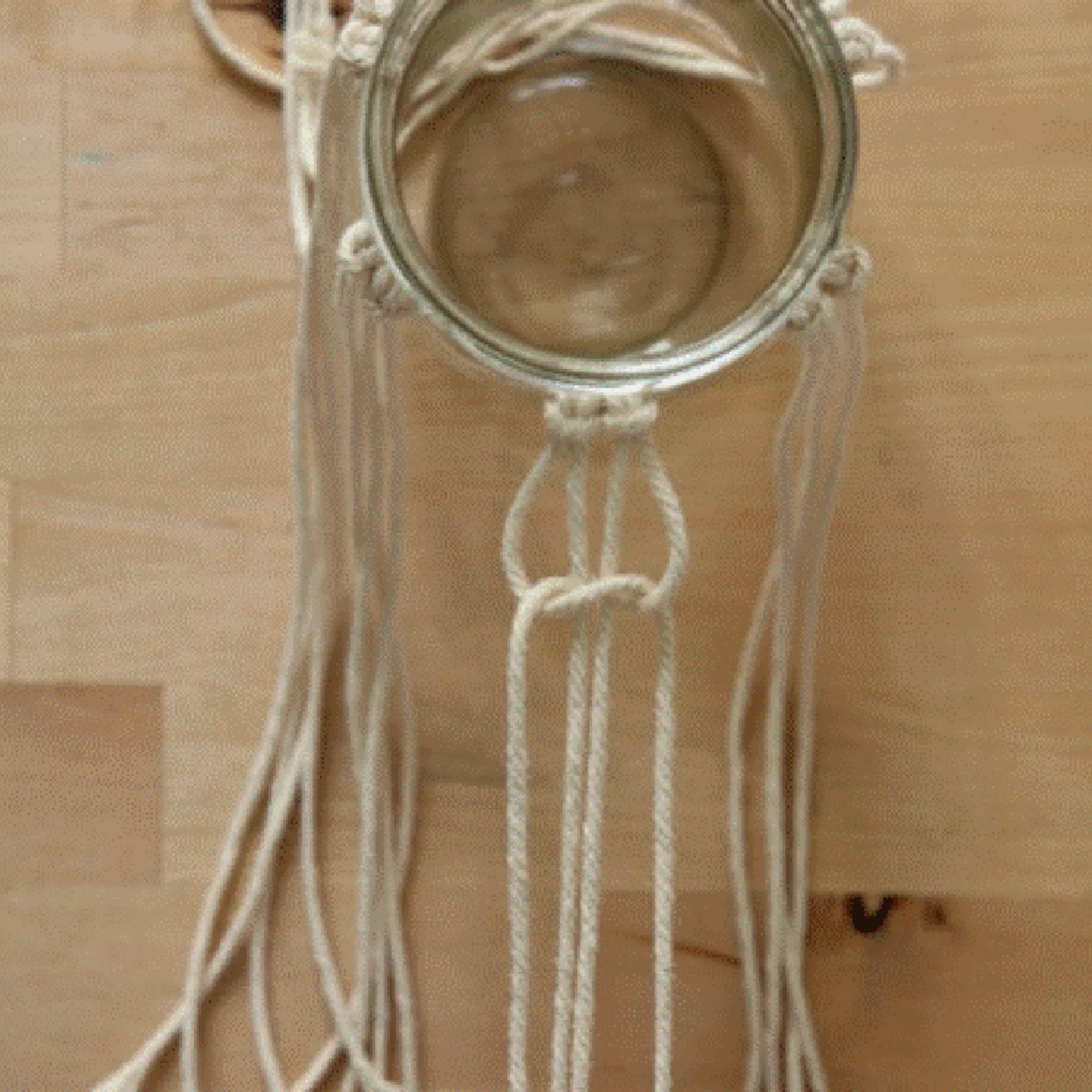 Ein Glas wird mit Makramee-Schnüren auf einem Holztisch dekoriert.