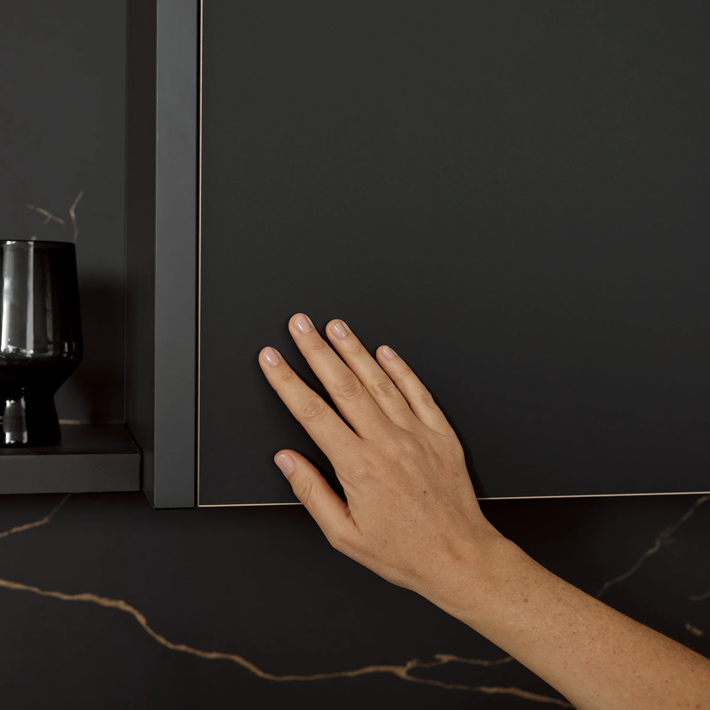 Eine Hand berührt einen eleganten schwarzen Küchenschrank. Nolte Küchen.