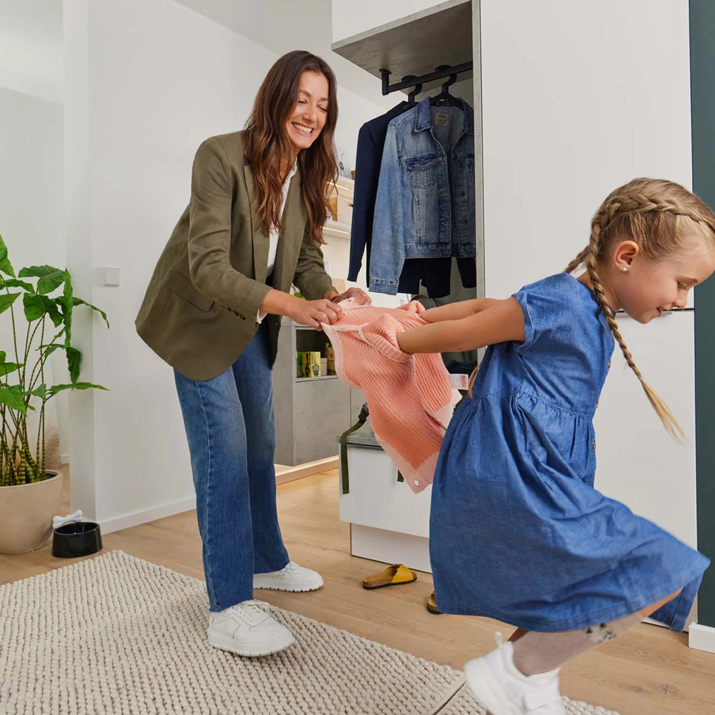 Eine Frau hilft einem spielenden Kind in einem modernen Wohnraum mit Nolte Living Möbeln.