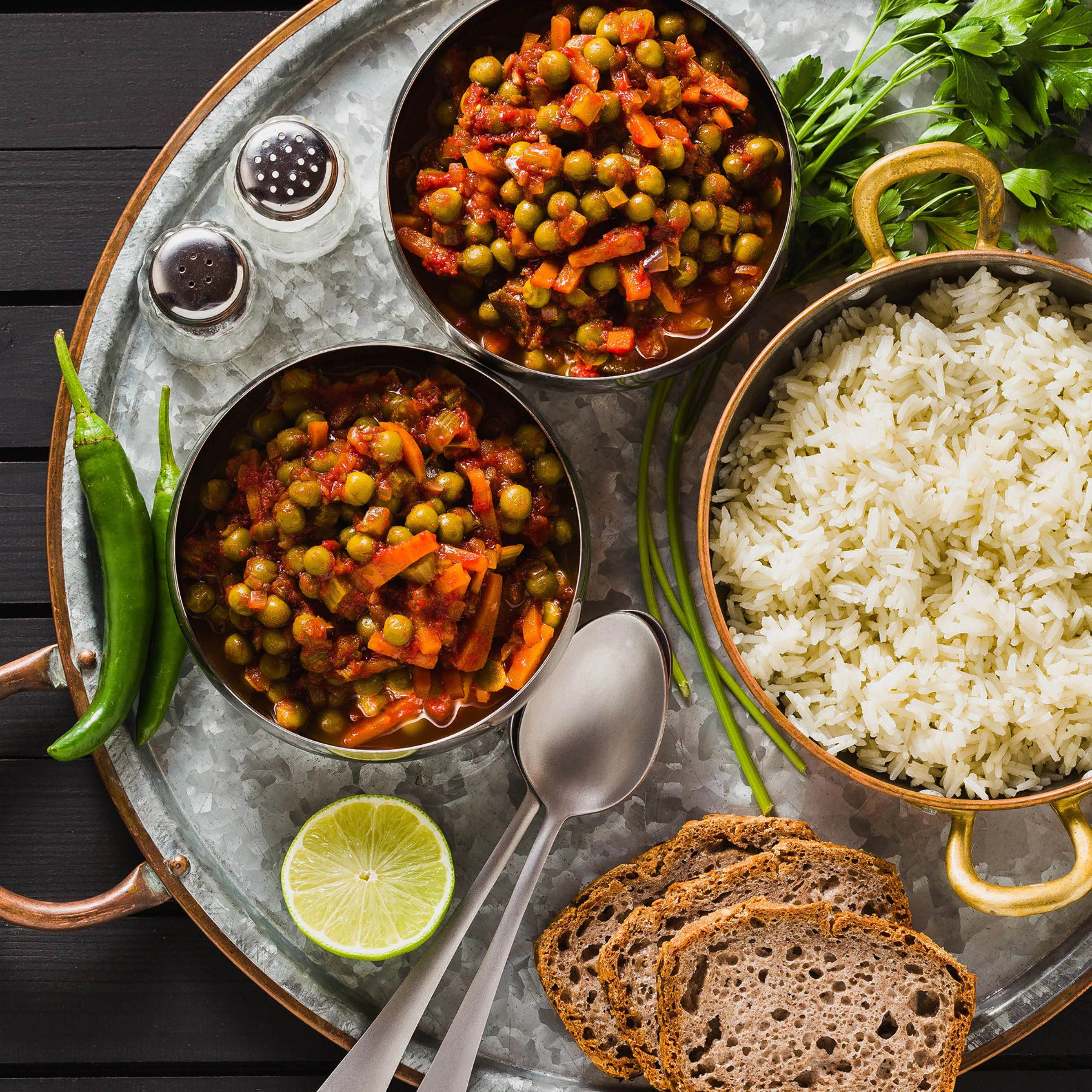 Eine Mahlzeit mit Erbsen-Curry, Reis, Brot, Limette und Gewürzen, appetitlich auf einem Tablett angerichtet.