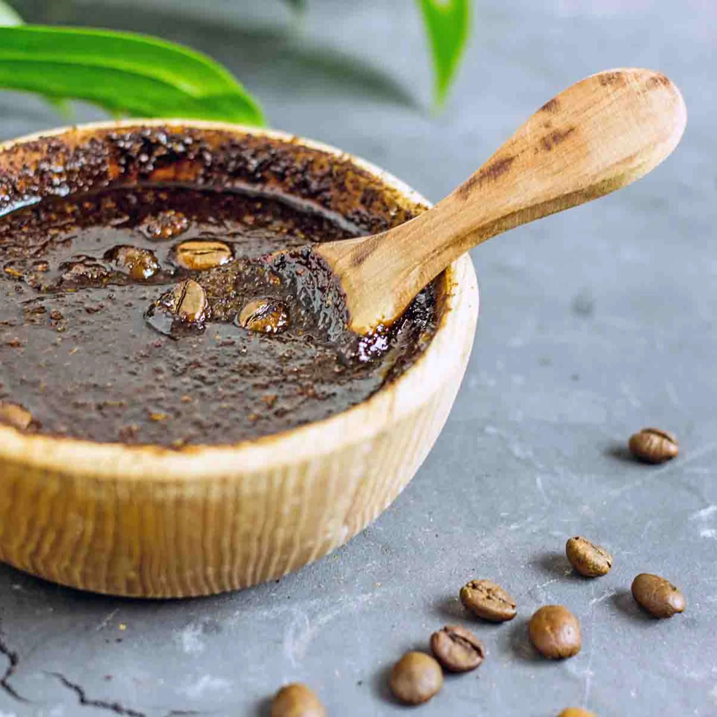 Eine Schale mit Kaffeesatz-Peeling und Kaffeebohnen liegt auf grauem Untergrund.