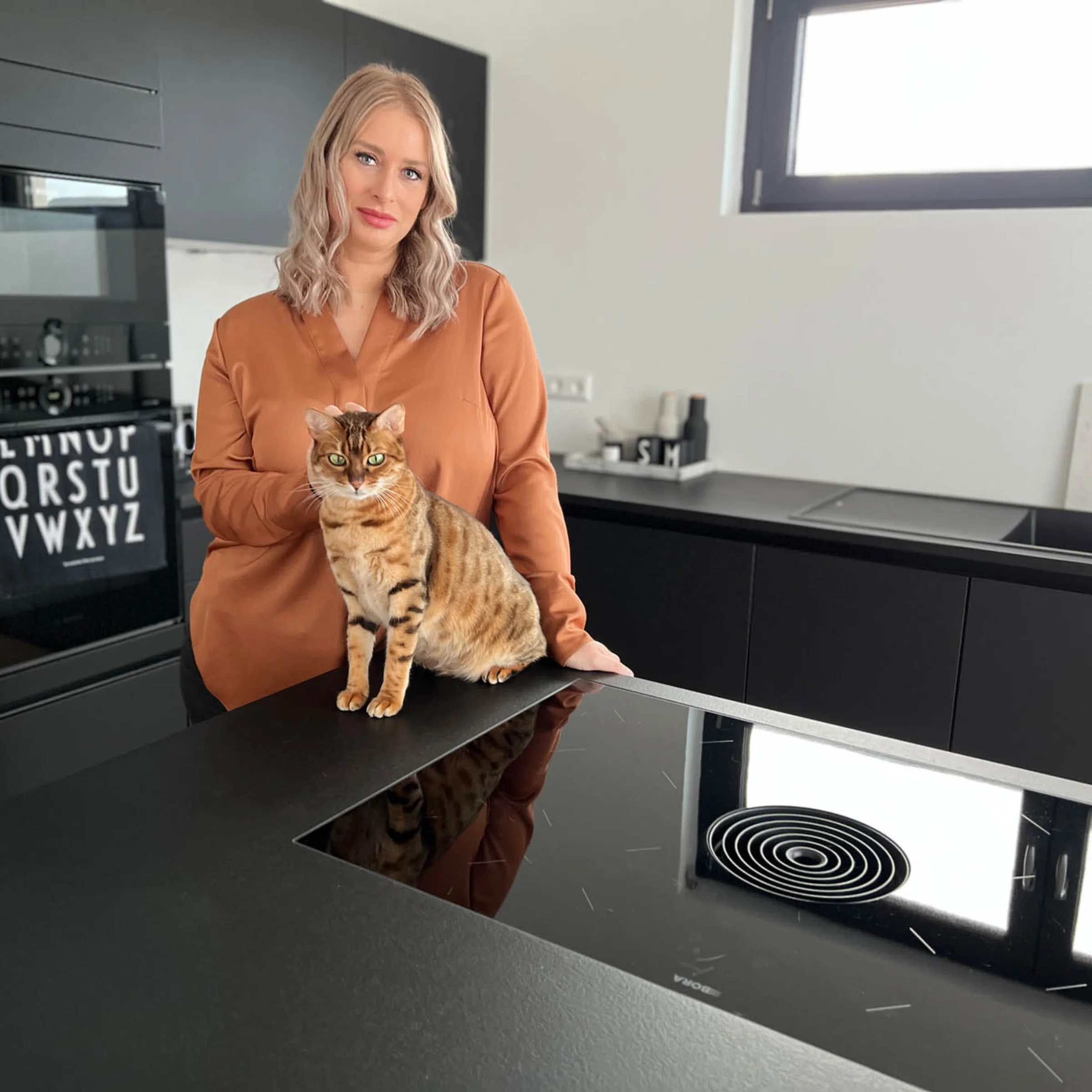 Eine Frau mit Katze in einer modernen Küche mit schwarzen Schränken. Nolte Küchen.