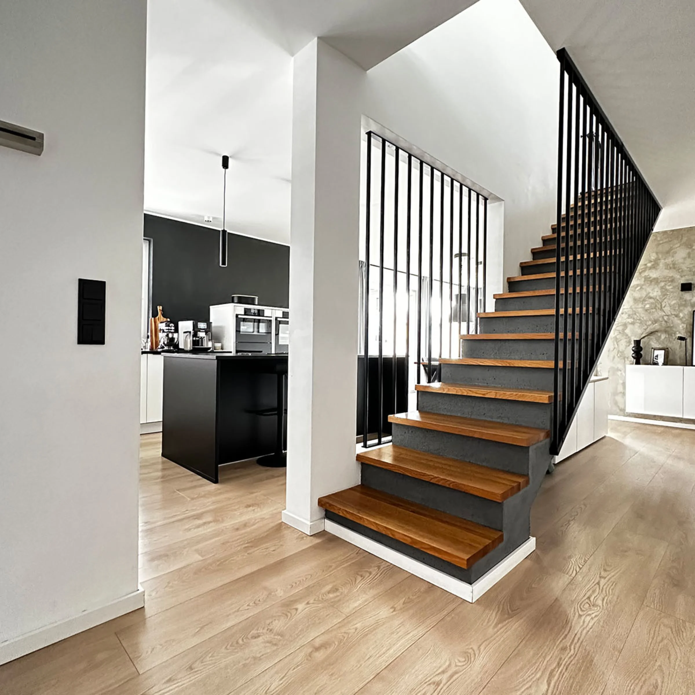 Eine moderne Küche mit schwarzer Wand und Insel, daneben eine Holztreppe. Nolte Küchen.