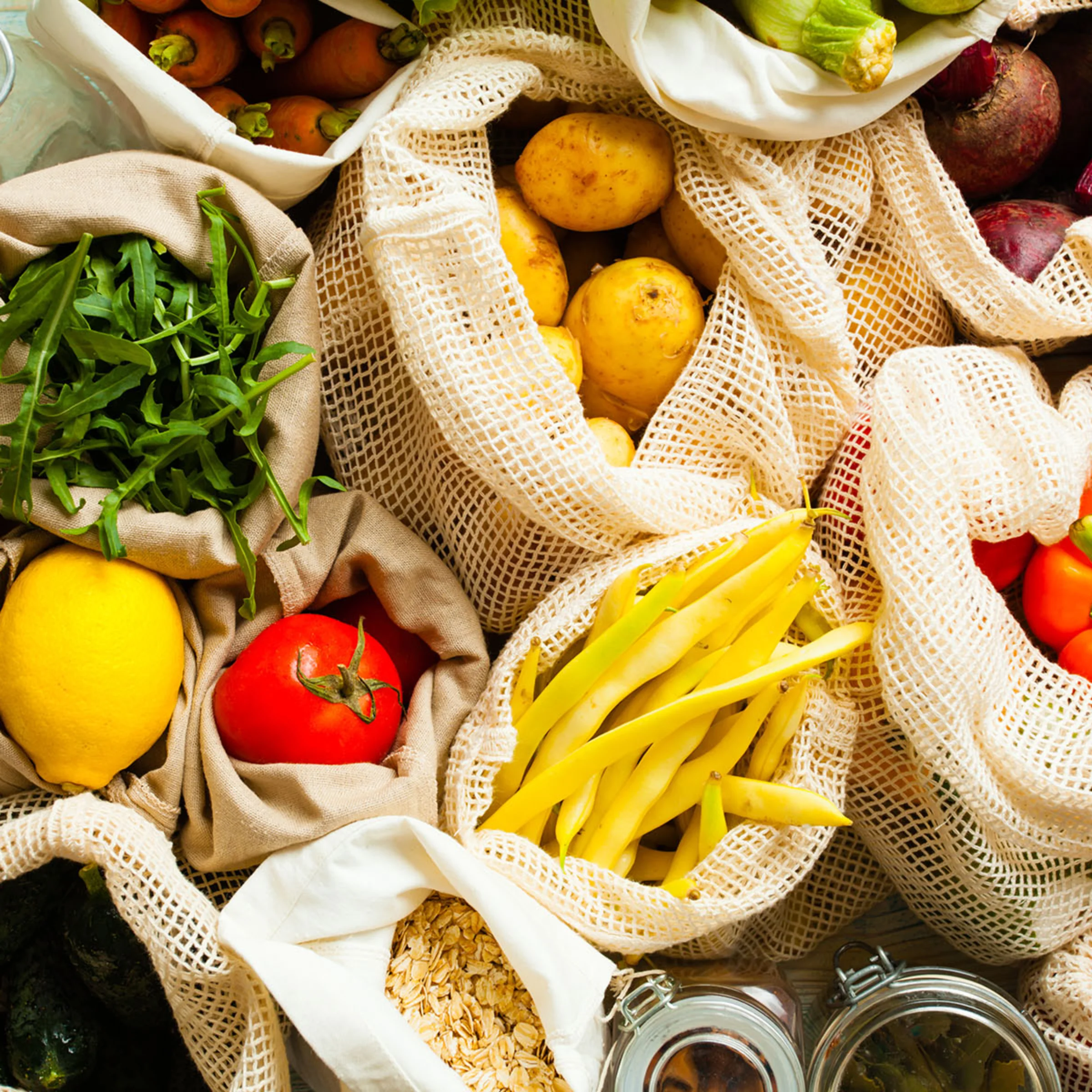 Various fresh vegetables and fruits in cloth bags on a table.