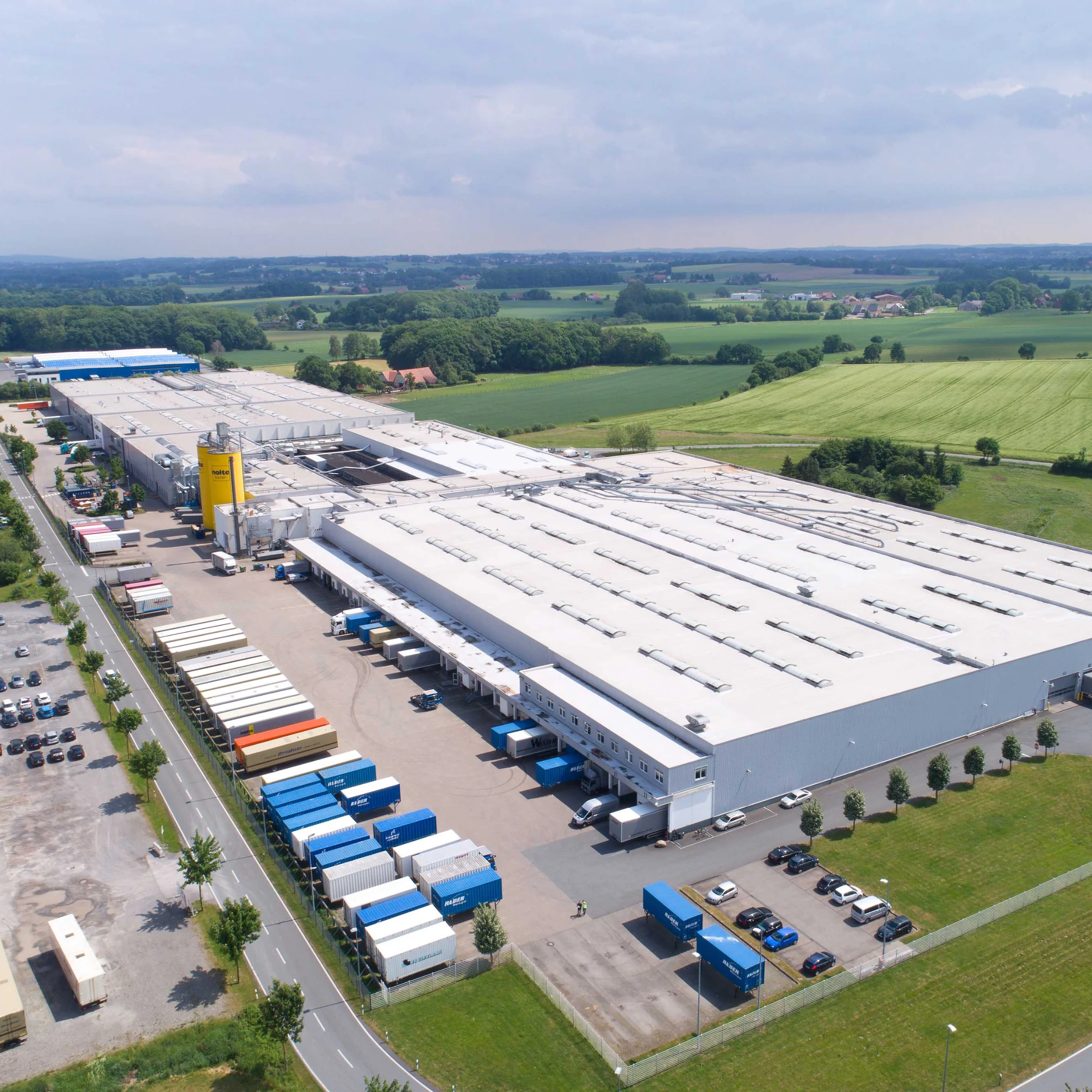 Eine große Industrieanlage auf dem Land, umgeben von Feldern; Nolte Küchen.