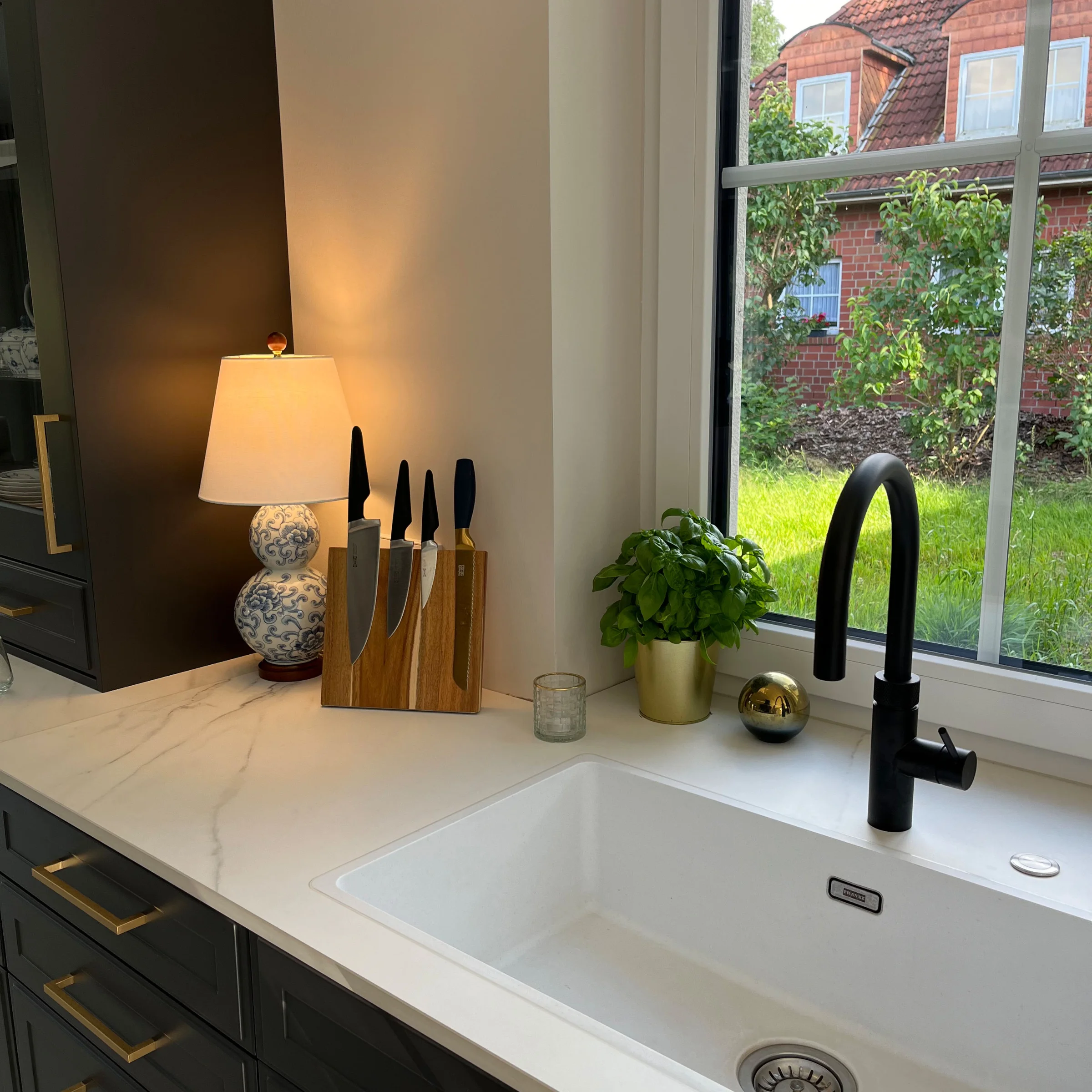 In einer modernen Küche mit weißer Spüle und Kräutertopf auf der Arbeitsplatte, gestaltet von Nolte Küchen.