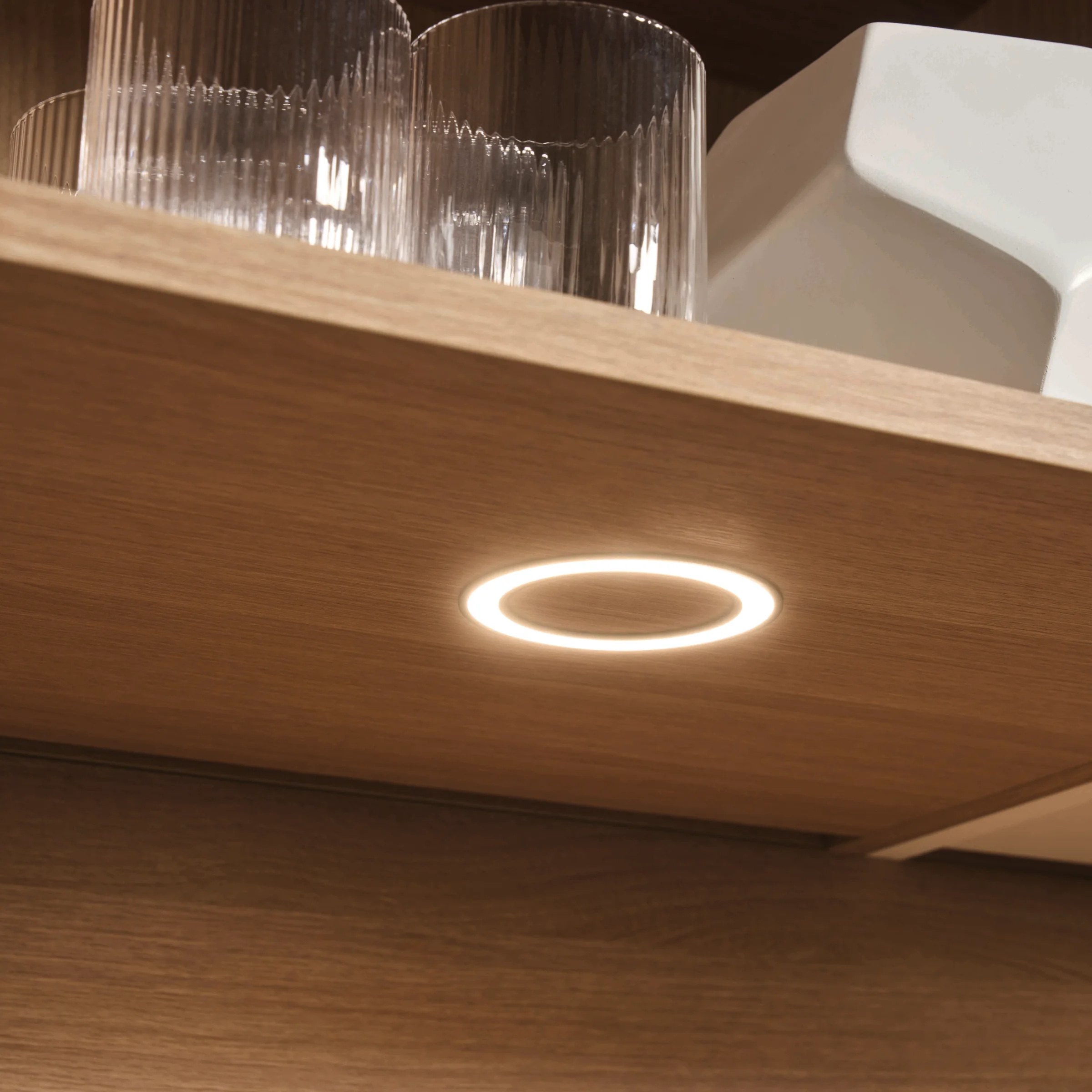 Ein beleuchteter Holz-Küchenschrank mit Gläsern und einer weißen Schale. Express Küchen.