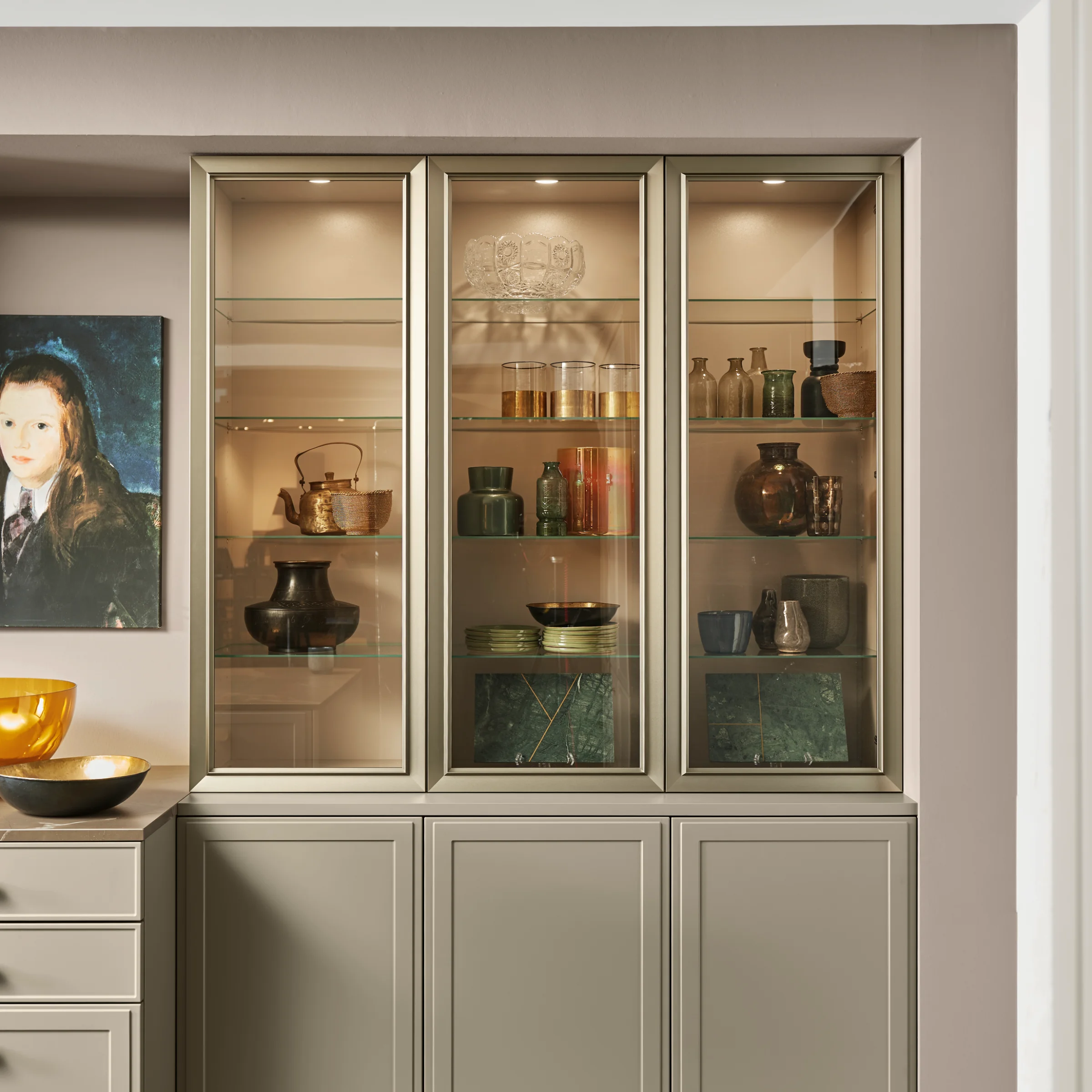Un aparador elegante con vitrina de vidrio, decorado con vajilla y arte, de Nolte Living.