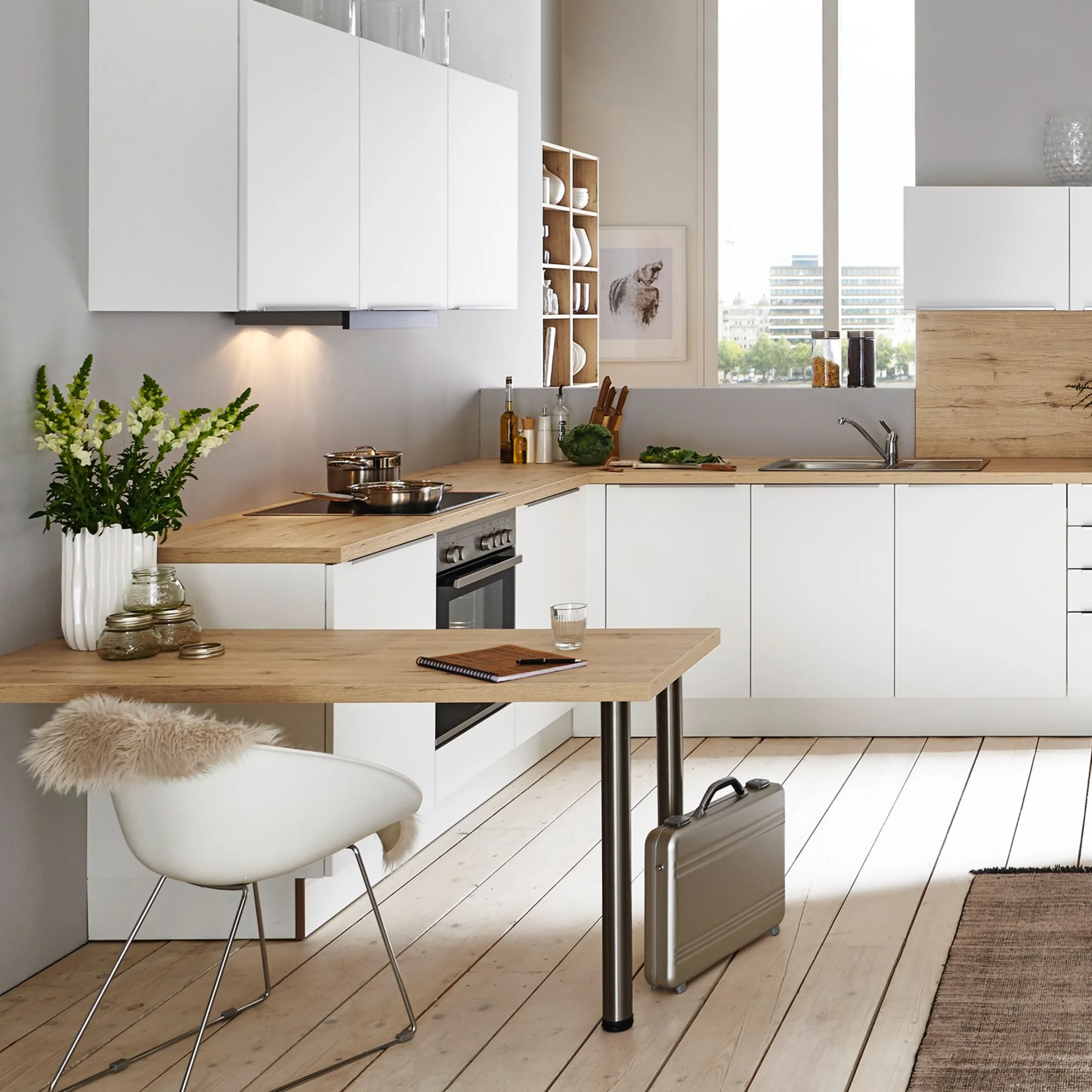 Helle Küche mit weißen Schränken und Holzdetails, links ein Tisch mit Stuhl, im Hintergrund ein Fenster. Nolte Küchen.