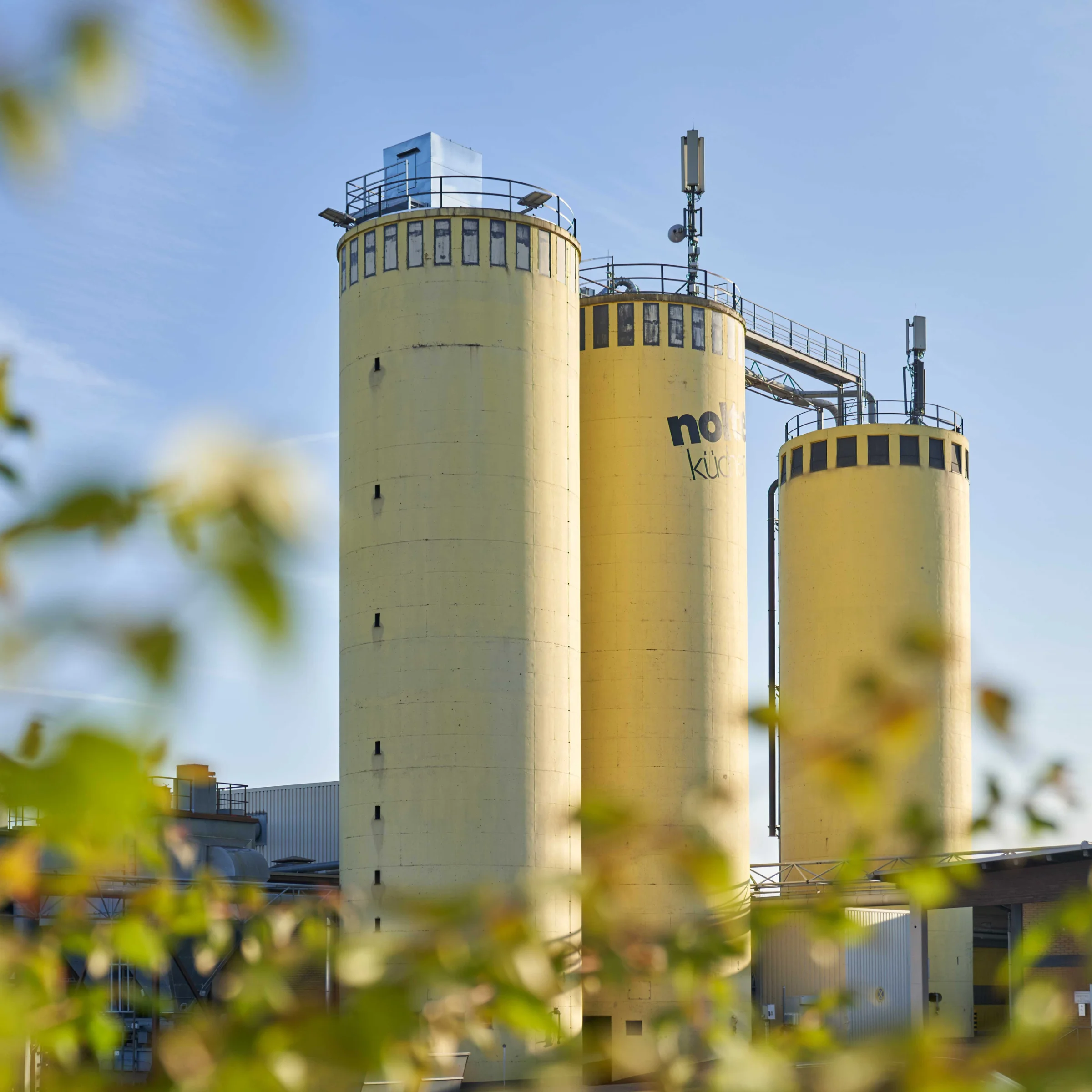 Drei große gelbe Silos mit der Aufschrift "Nolte Küchen" stehen vor einem klaren Himmel.