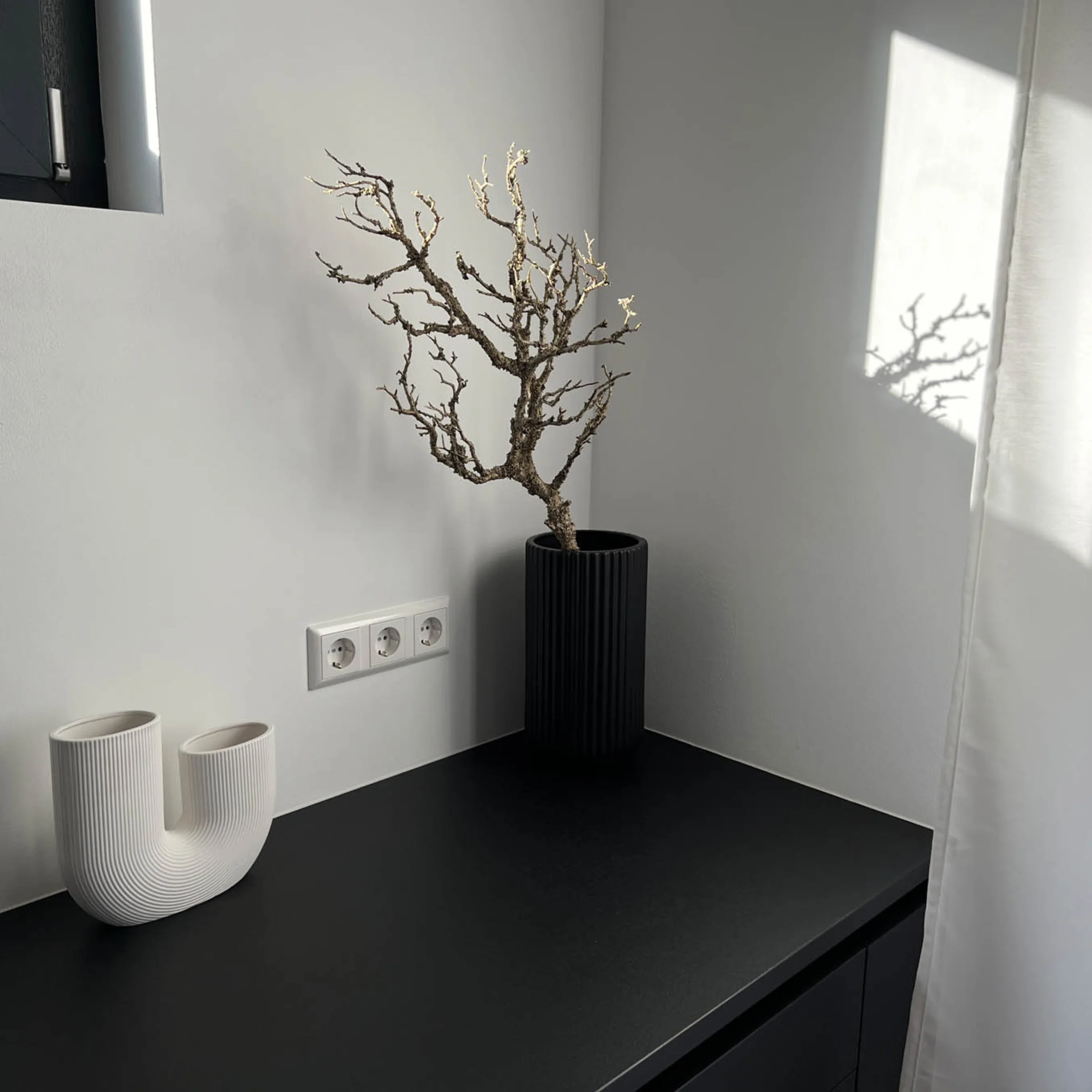 Auf der schwarzen Arbeitsplatte stehen eine weiße Vase und eine schwarze Vase mit einem Zweig, passend zu Nolte Living.