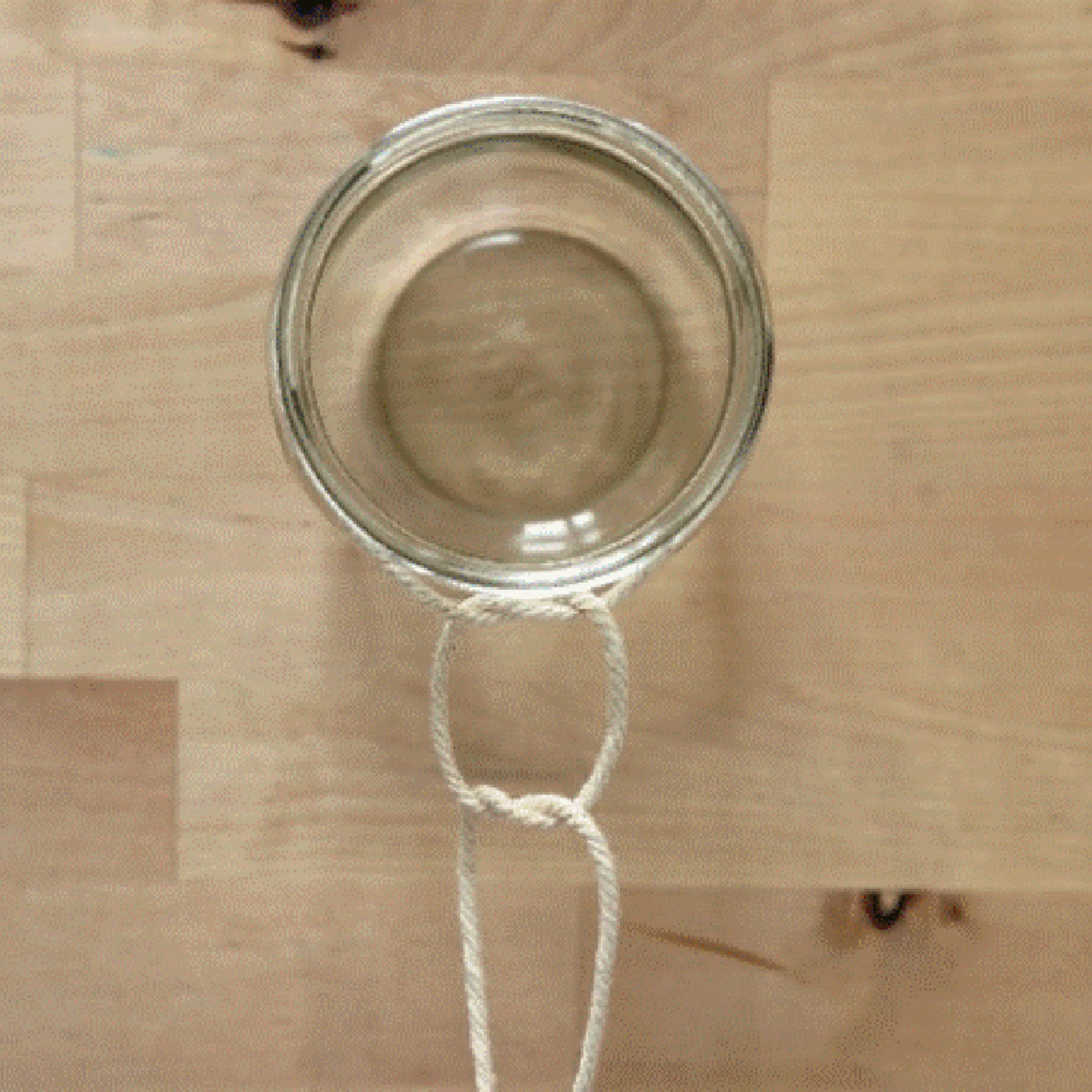 Ein Glas wird mit einem Seil zu einem hängenden Behälter gebunden.