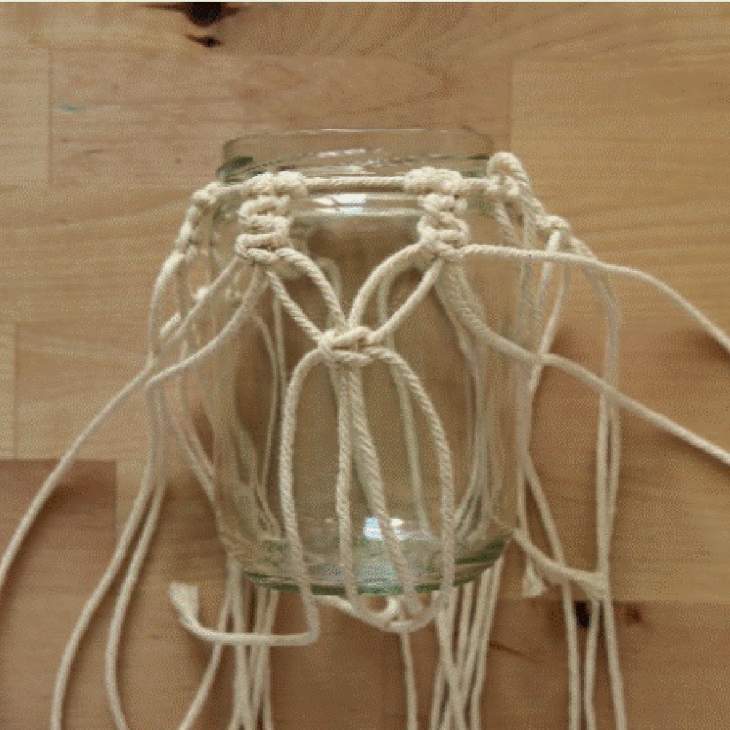 Ein Glasgefäß mit Makramee-Halterung auf einem Holztisch.