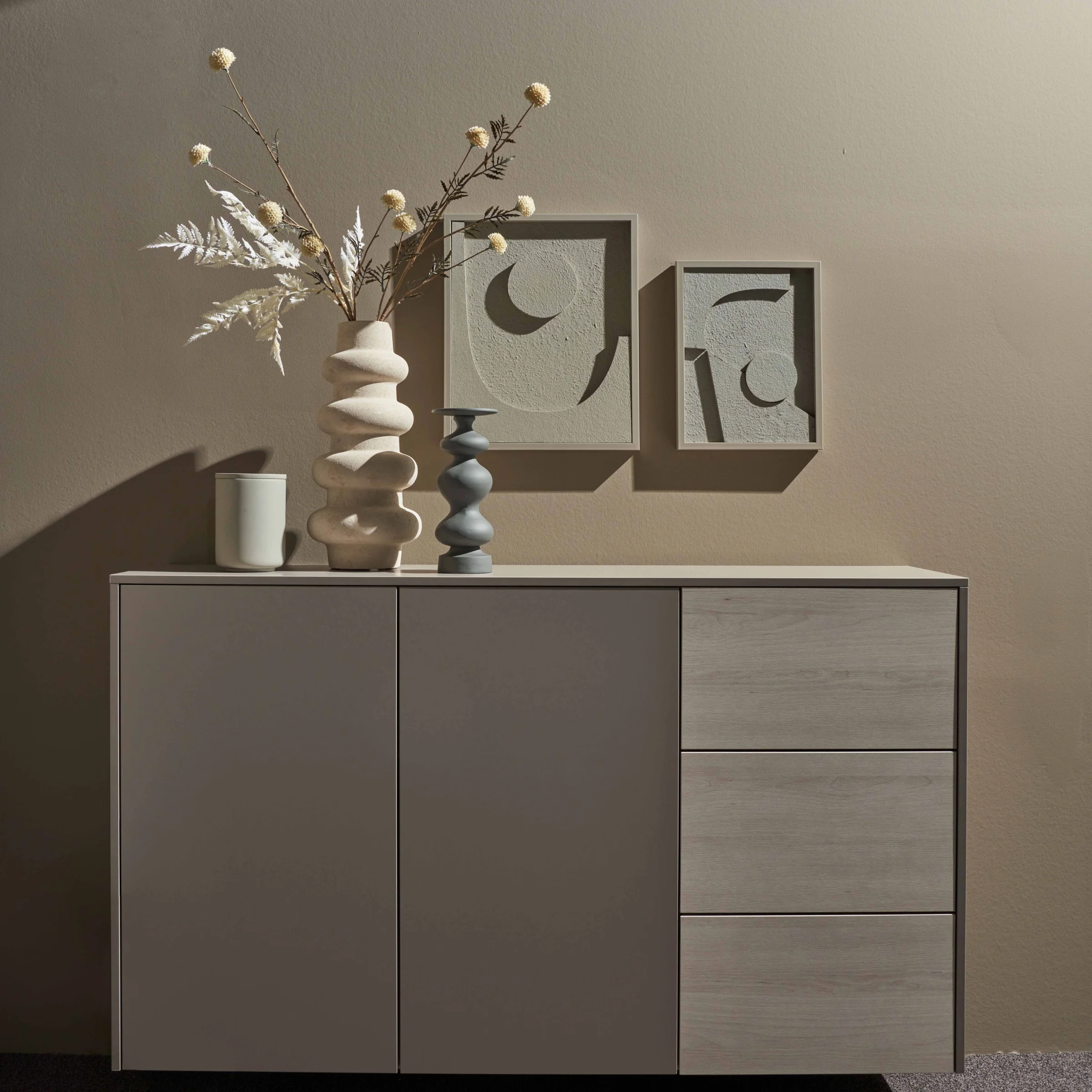 Ein Sideboard mit dekorativen Vasen und Kunstwerken an der Wand, Nolte Living.