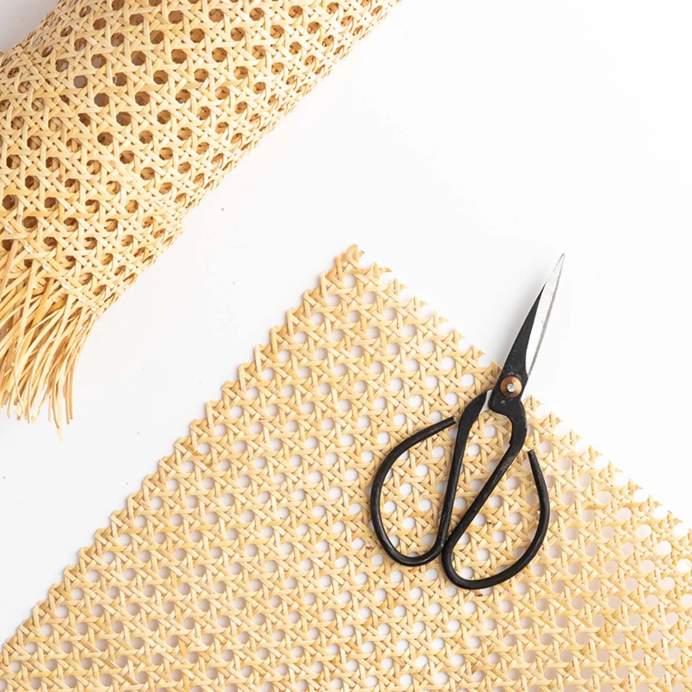 Scissors next to a piece of braided raffia on a white background.