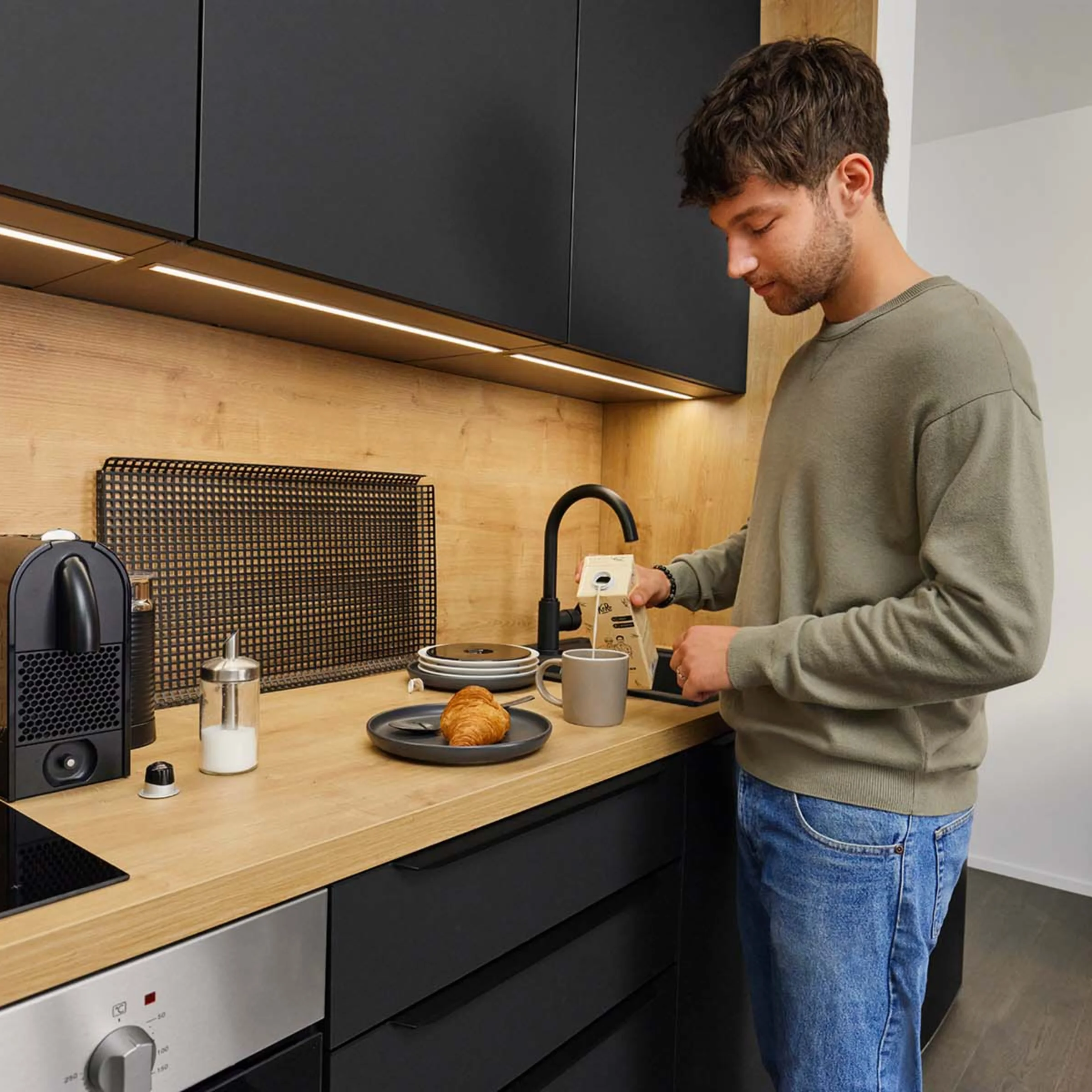 Ein Mann bereitet in einer modernen Küche mit Holz- und Schwarzakzenten Kaffee zu. Nolte Küchen.