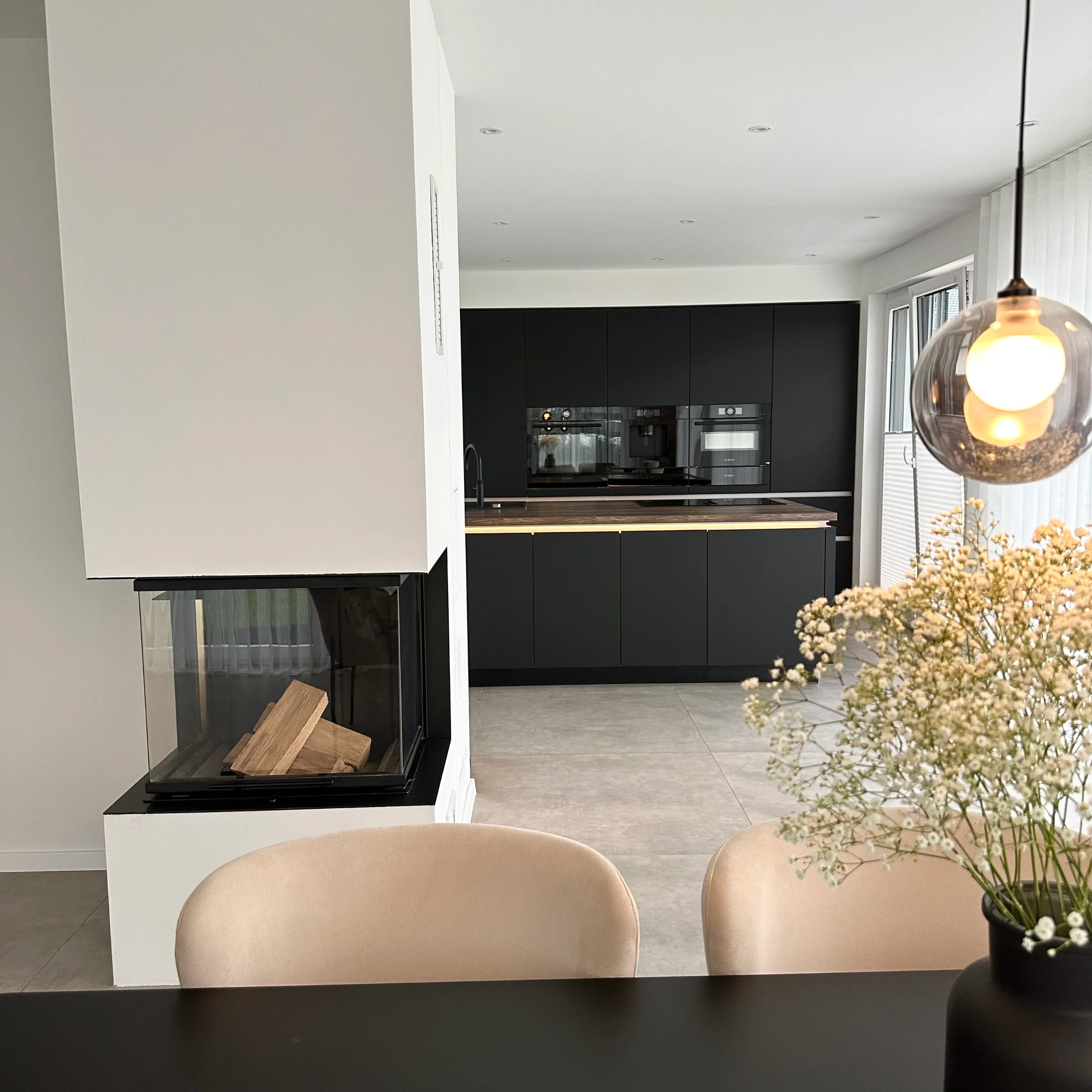 Eine moderne Küche mit schwarzer Einrichtung und Kamin, im Vordergrund ein Esstisch. Nolte Küchen.