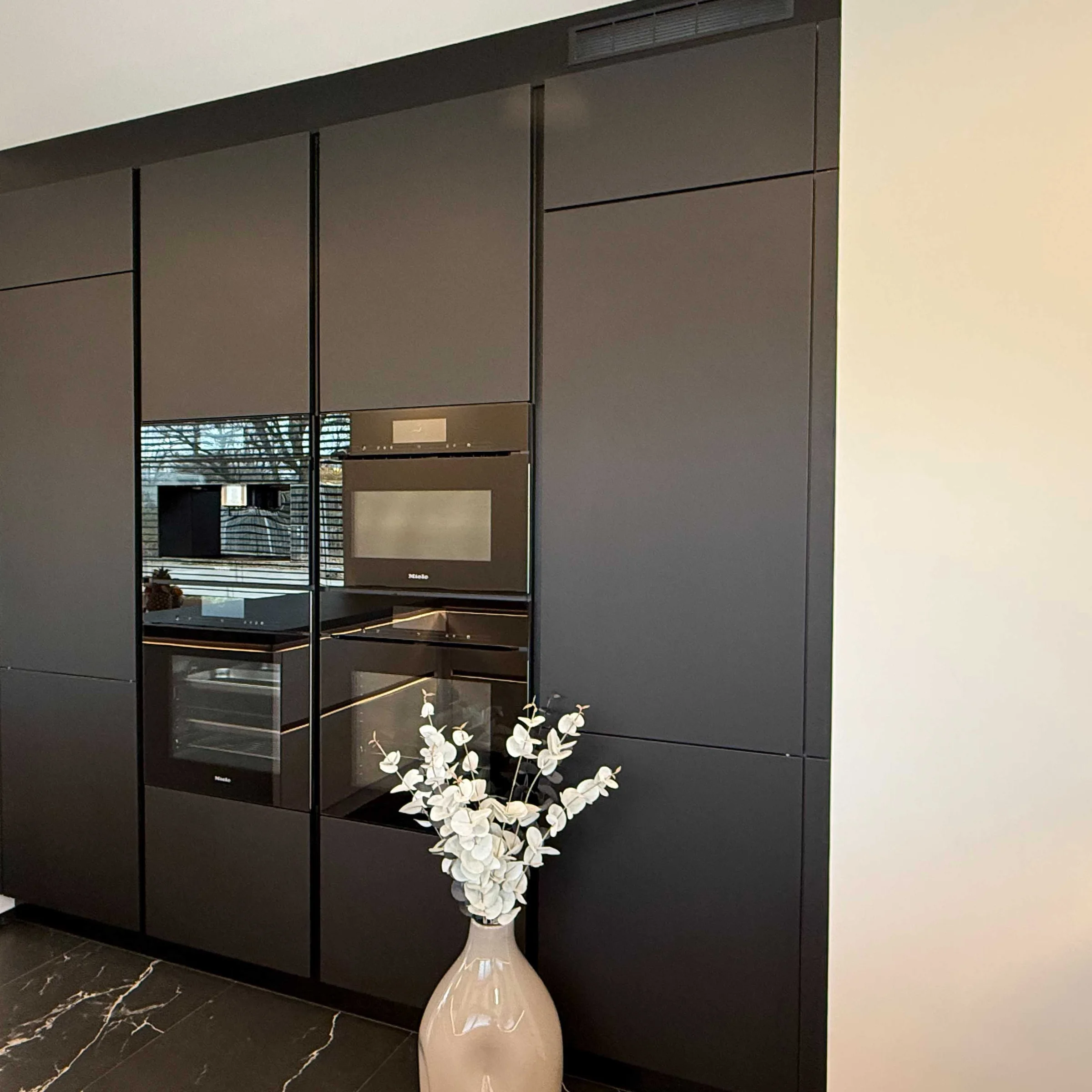 Eine moderne schwarze Einbauküche mit einem Strauß weißer Blumen, Nolte Küchen.