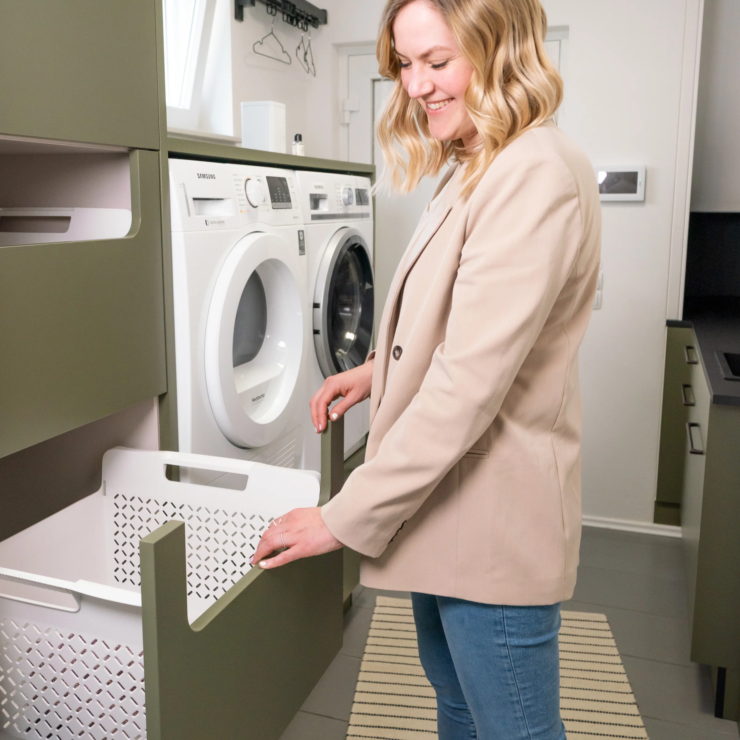 Eine Frau steht in einem modernen Hauswirtschaftsraum mit Waschmaschine und Trockner von Nolte Hauswirtschaftsräume.