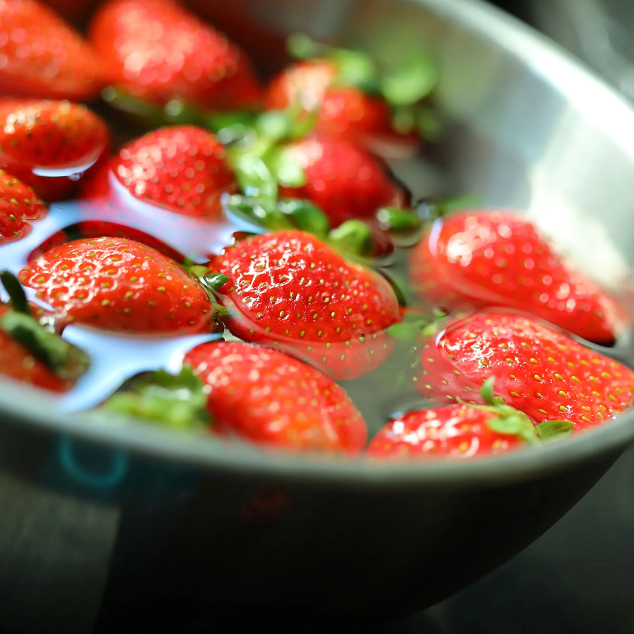 Erdbeeren schwimmen in einer mit Wasser gefüllten Metallschüssel.