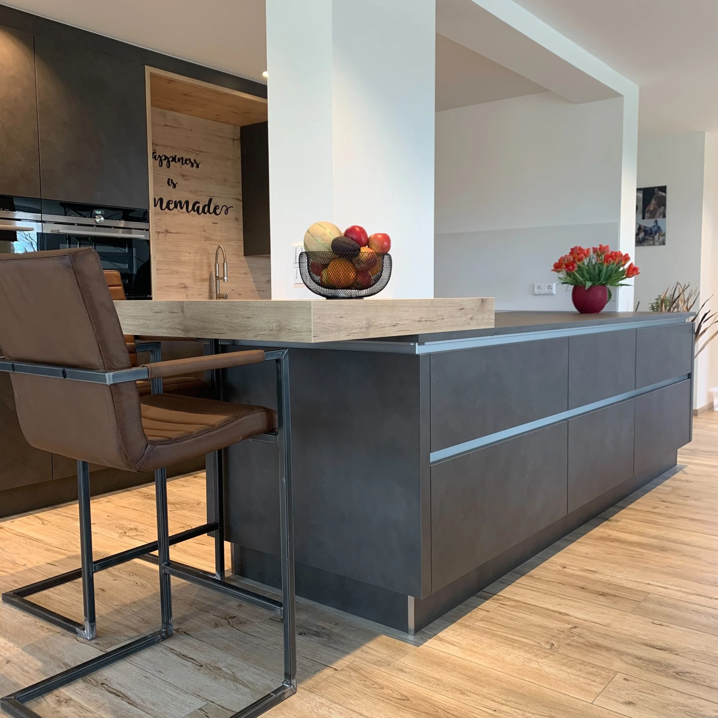 Moderne Küche mit dunkler Insel und Obstschale auf Holztheke, im Hintergrund Nolte Küchen.
