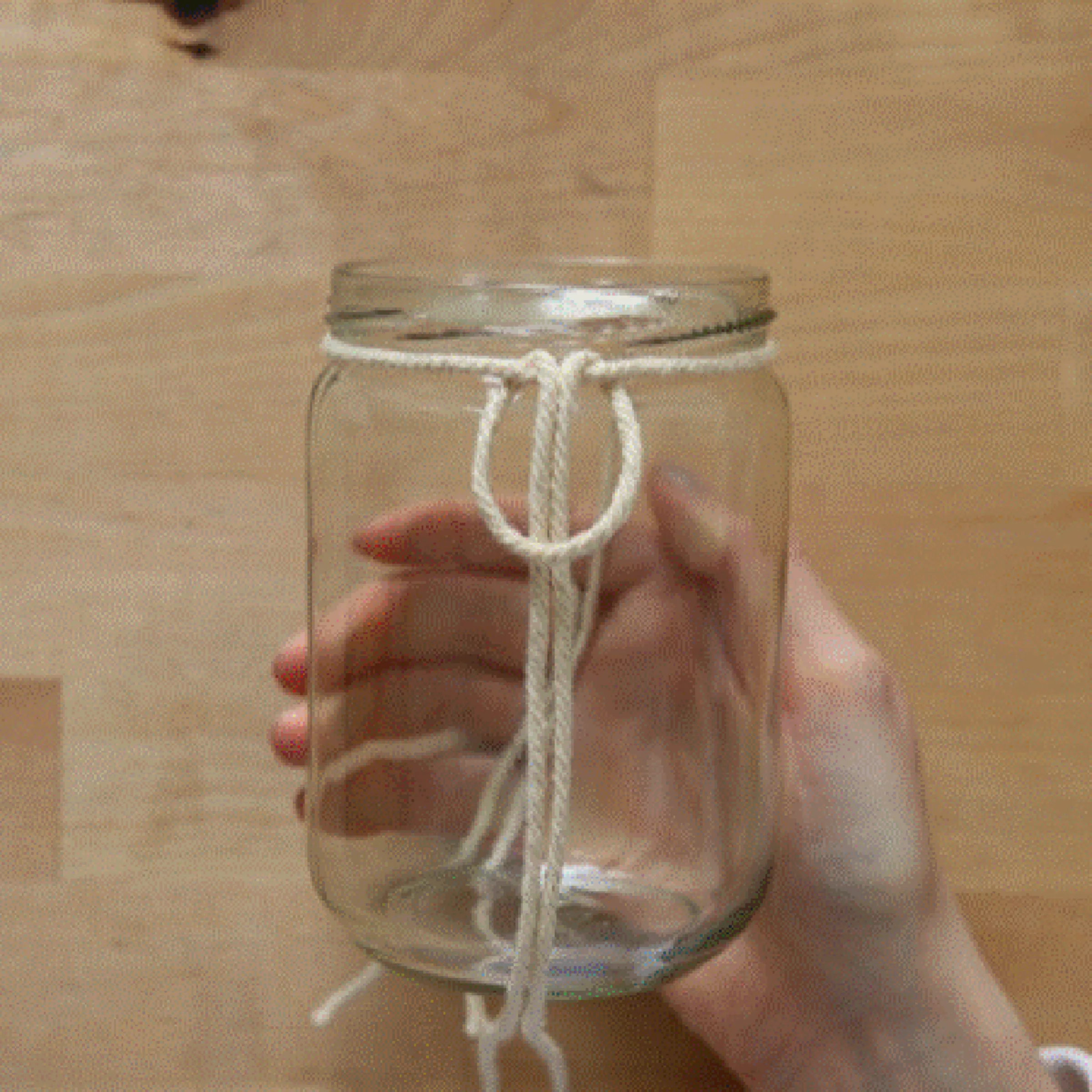 Eine Hand knotet ein Seil um ein leeres Einmachglas.