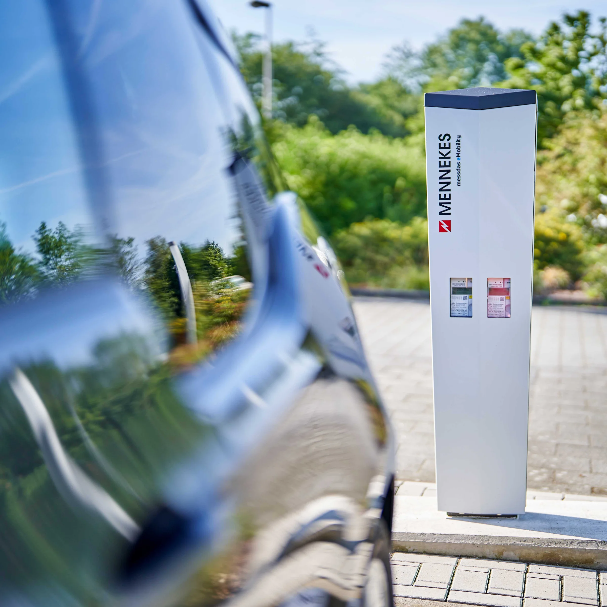 Ein Elektroauto steht vor einer Ladestation im Freien, umgeben von Bäumen. Nolte Küchen.