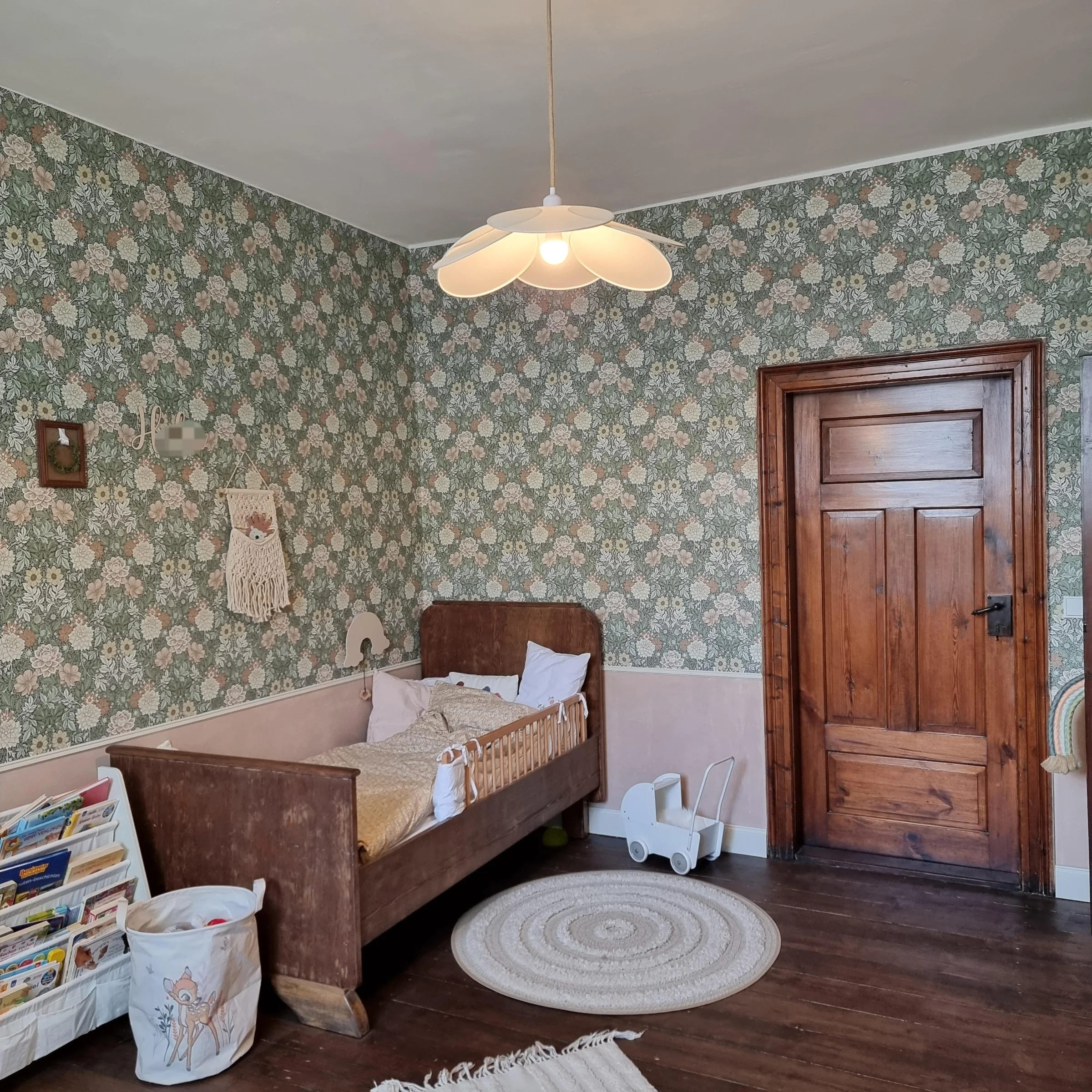 Un dormitorio infantil con cama de madera, papel tapiz de flores y alfombra redonda sobre suelo de madera.