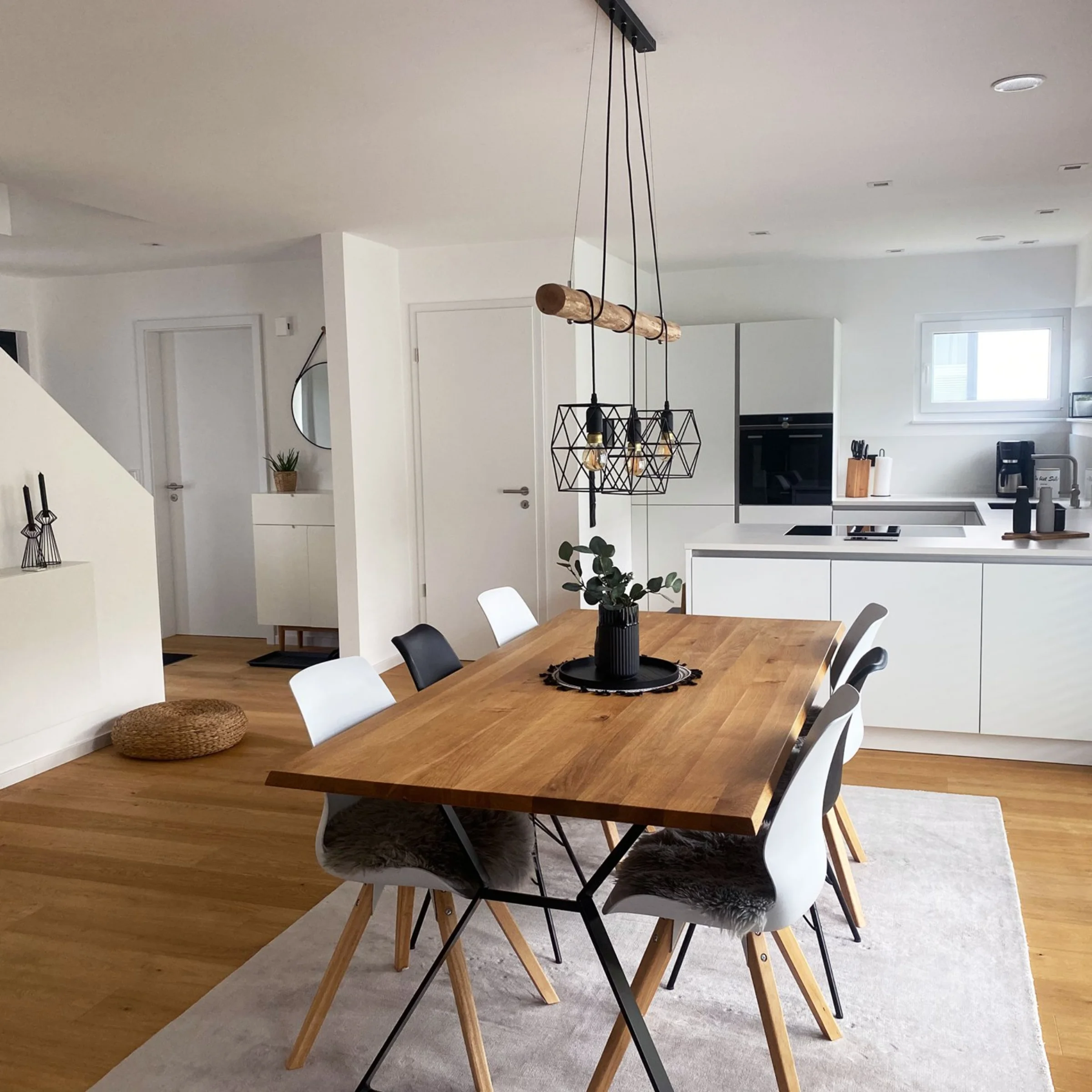 Ein moderner Essbereich mit Holztisch und weißen Stühlen neben einer offenen Küche von Nolte Küchen.