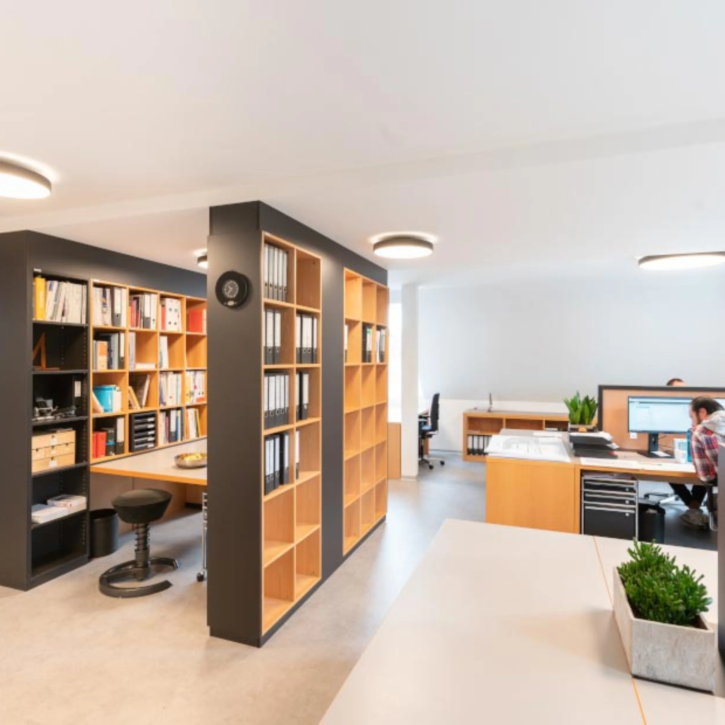 Ein modernes Büro mit Regalen und Schreibtischen, die eine organisierte Arbeitsumgebung schaffen.