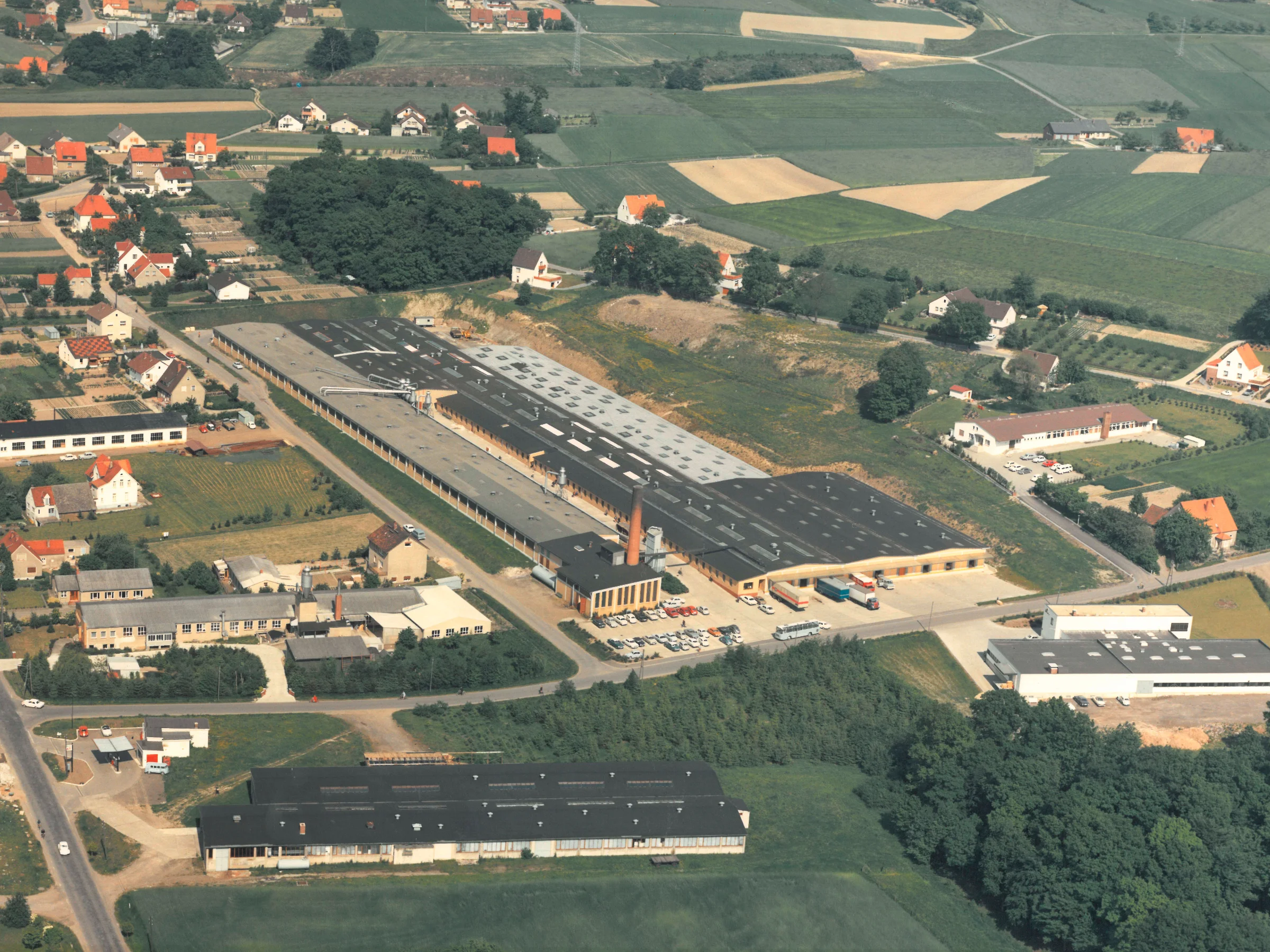 In einer ländlichen Umgebung sind Fabrikgebäude von Nolte zu sehen, umgeben von Feldern und kleinen Siedlungen.