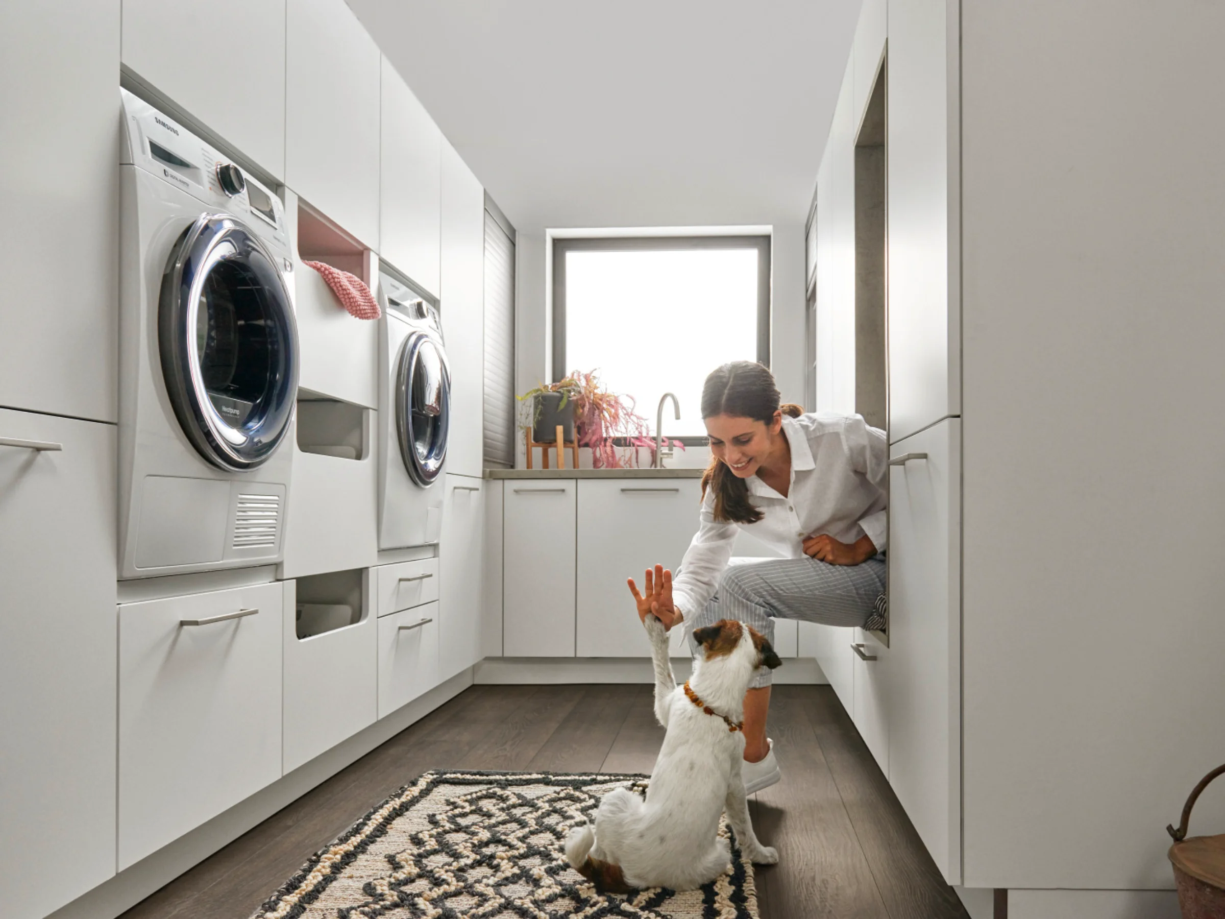 Eine Frau spielt mit einem Hund in einem modernen Hauswirtschaftsraum von Nolte Hauswirtschaftsräume.