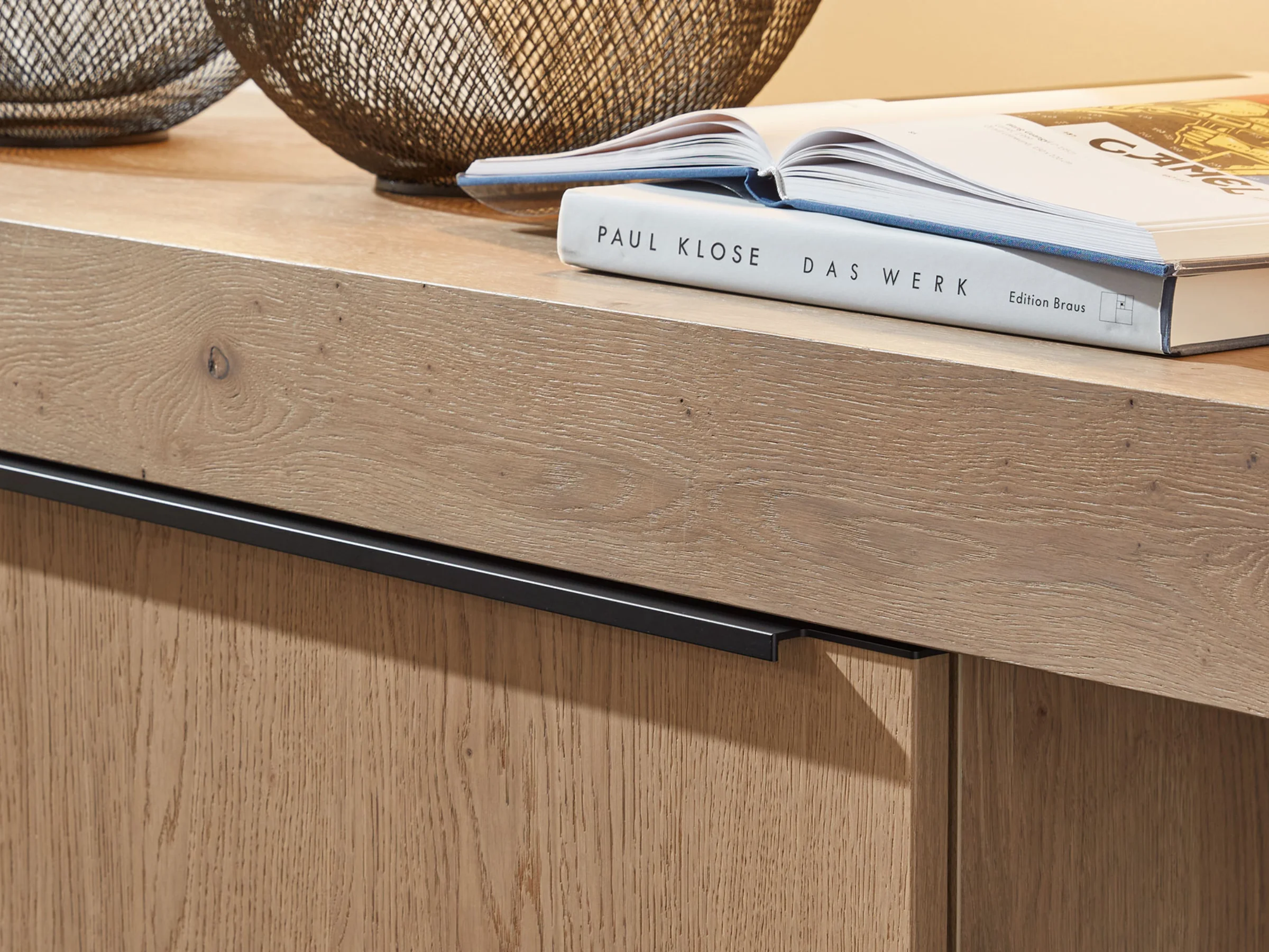 Ein Holzschrank mit Büchern und Drahtkörben darauf gehört zur Serie Nolte Living.