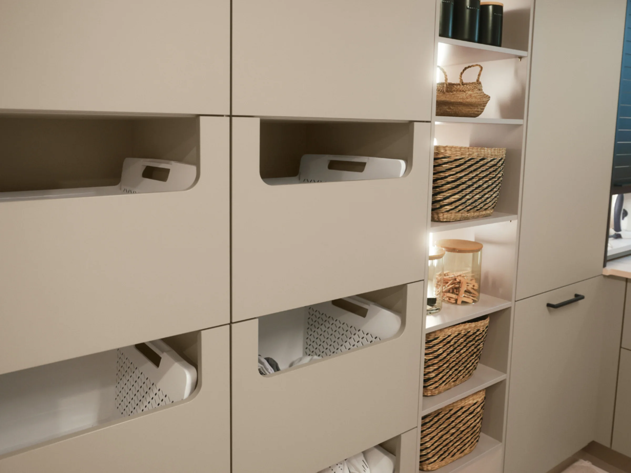 Ein Hauswirtschaftsraum mit beige Schränken und Körben, präsentiert von Nolte Hauswirtschaftsräume.