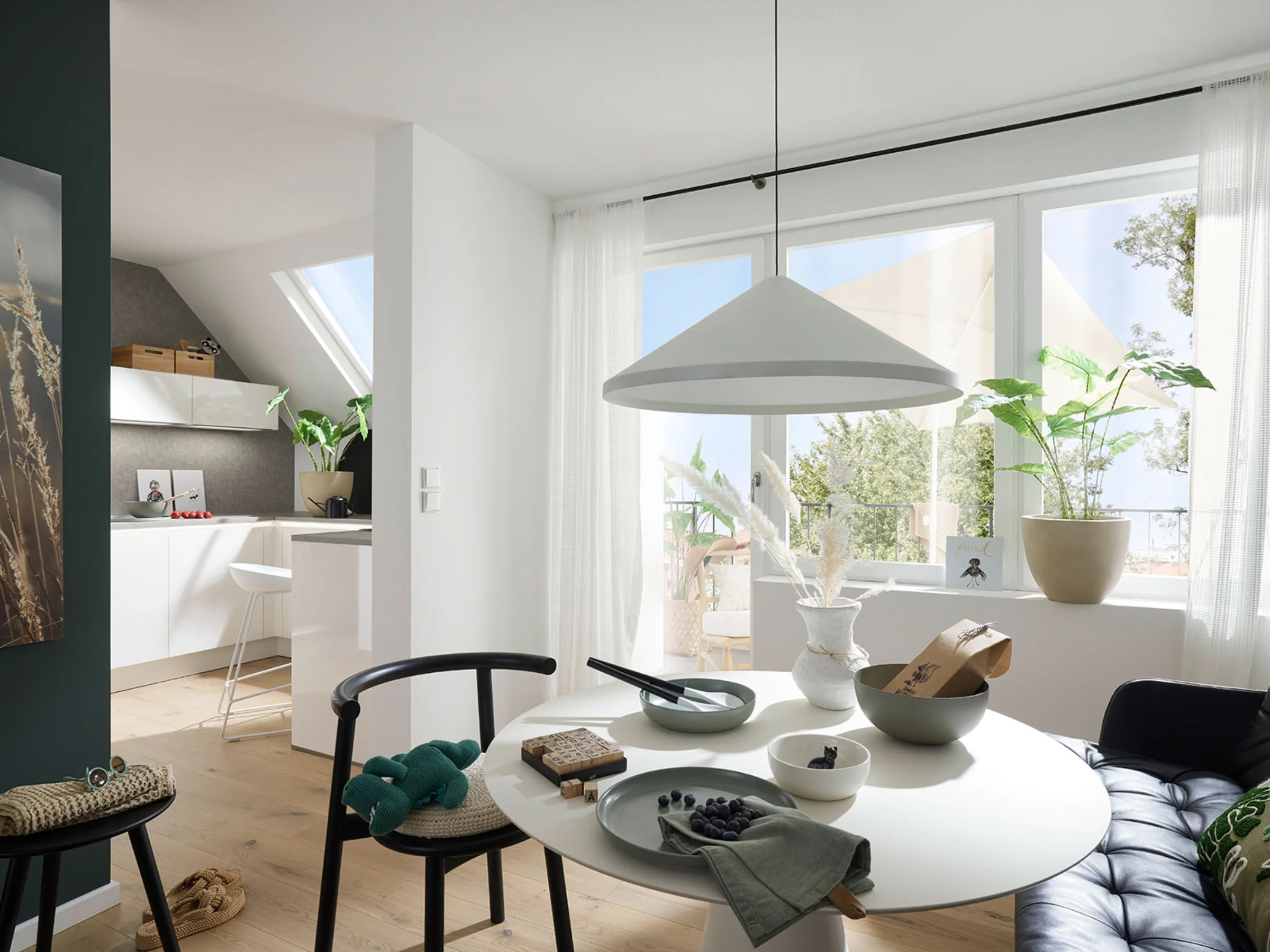 Ein heller Wohnbereich mit Esstisch und Küchenzeile, umgeben von Pflanzen, präsentiert Nolte Living.