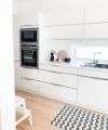 Eine moderne, helle Küche mit weißen Schränken und einem Teppich, stilvoll von Nolte Küchen gestaltet.