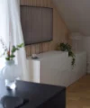 A modern living room features a white sideboard with plants, beneath a wall-mounted TV. Nolte Living.