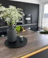 In einer modernen Küche mit dunklen Schränken steht eine Vase mit Blumen auf der Arbeitsplatte. Nolte Küchen.