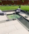 Ein moderner Garten mit Wasserbecken und Sitzbereich, umgeben von gepflegtem Rasen und Pflanzen.
