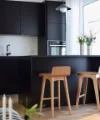 A modern kitchen with black cabinets and wooden chairs, designed by Nolte Kitchen.