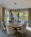 Ein eleganter Essbereich mit rundem Holztisch und Polsterstühlen unter einem Kronleuchter. Nolte Living.
