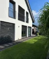 Ein modernes Haus mit großen Fenstern und gepflegtem Rasen an einem sonnigen Tag.
