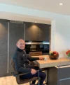 Cucina moderna con uomo al bancone, ciotola di frutta e fiori, design di Nolte Kitchen.