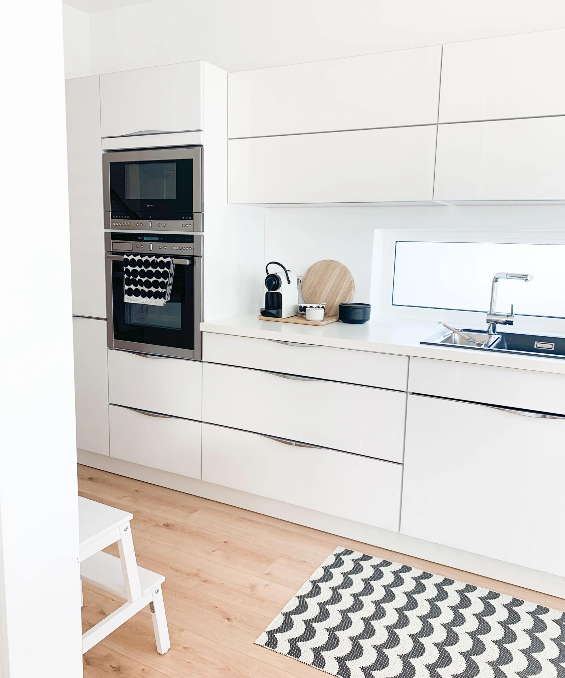 Eine moderne, helle Küche mit weißen Schränken und einem Teppich, stilvoll von Nolte Küchen gestaltet.