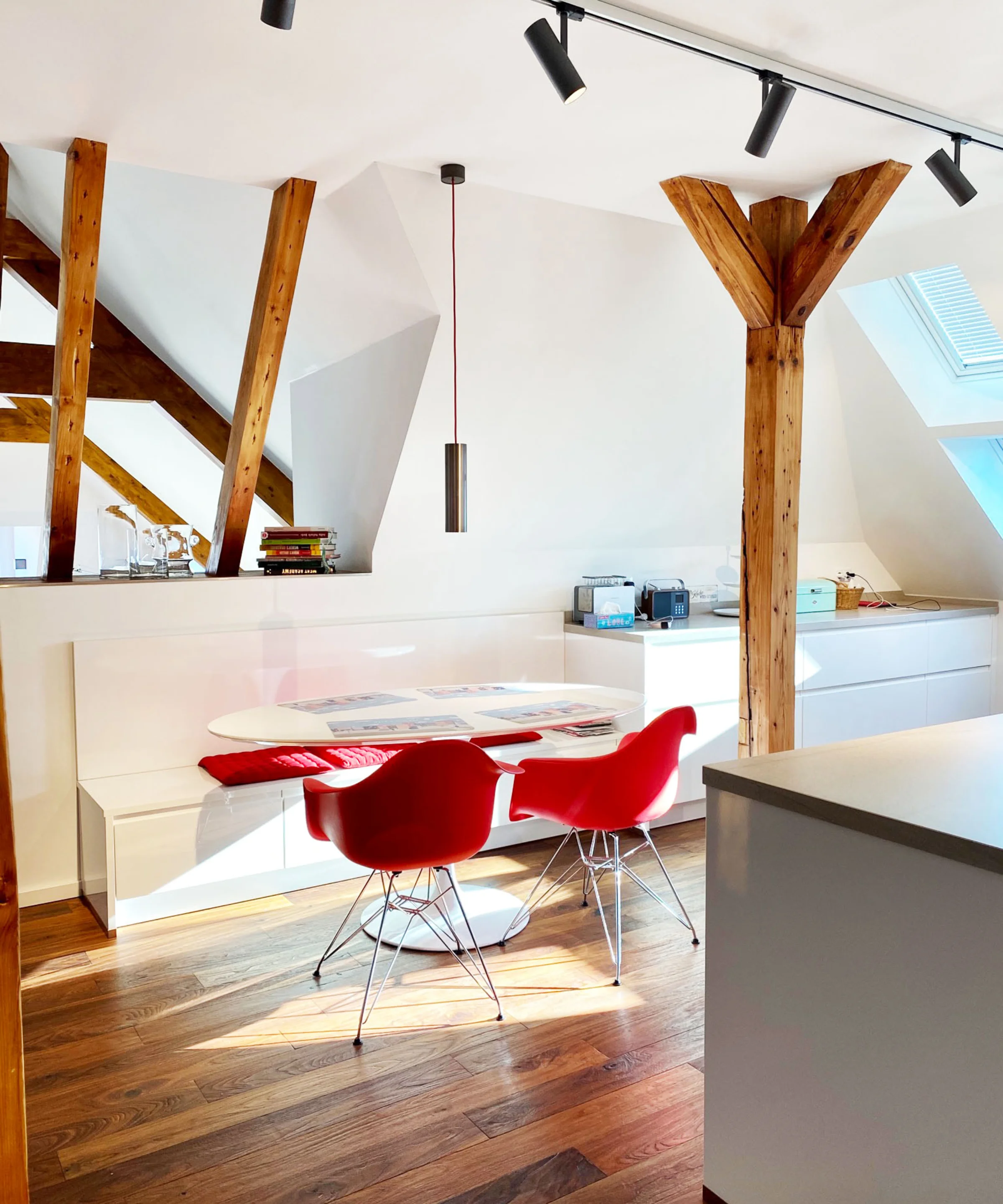 Eine moderne Küche mit Holzbalken und roten Stühlen unter einem Dachfenster. Nolte Küchen.